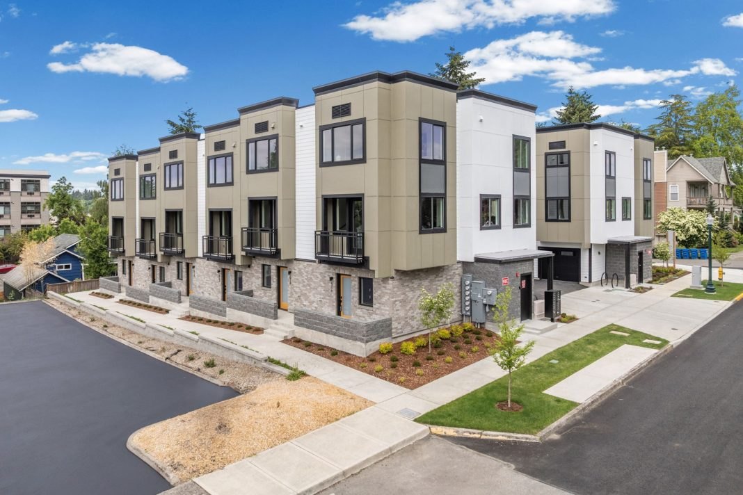 A row of modern three-story townhomes with stone and panel exteriors along a paved street.