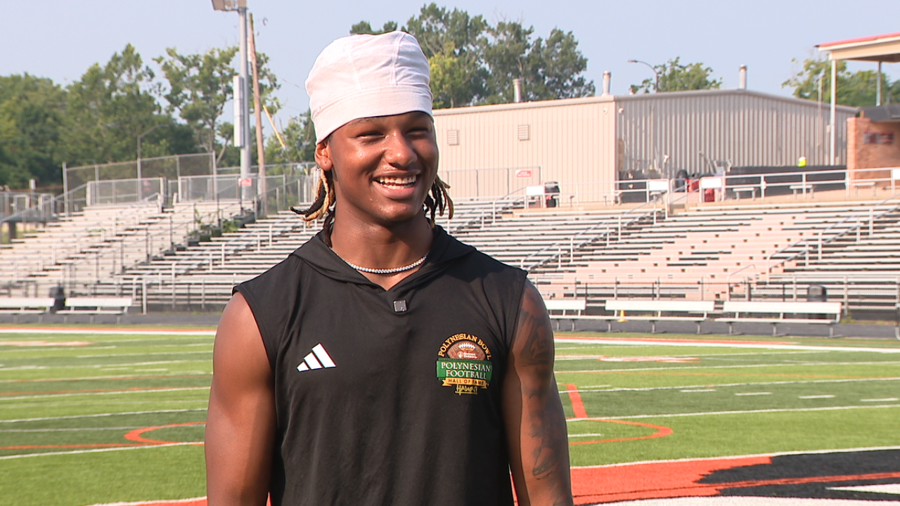 Young male athlete in a Polynesian Bowl hoodie smiling on a football field.