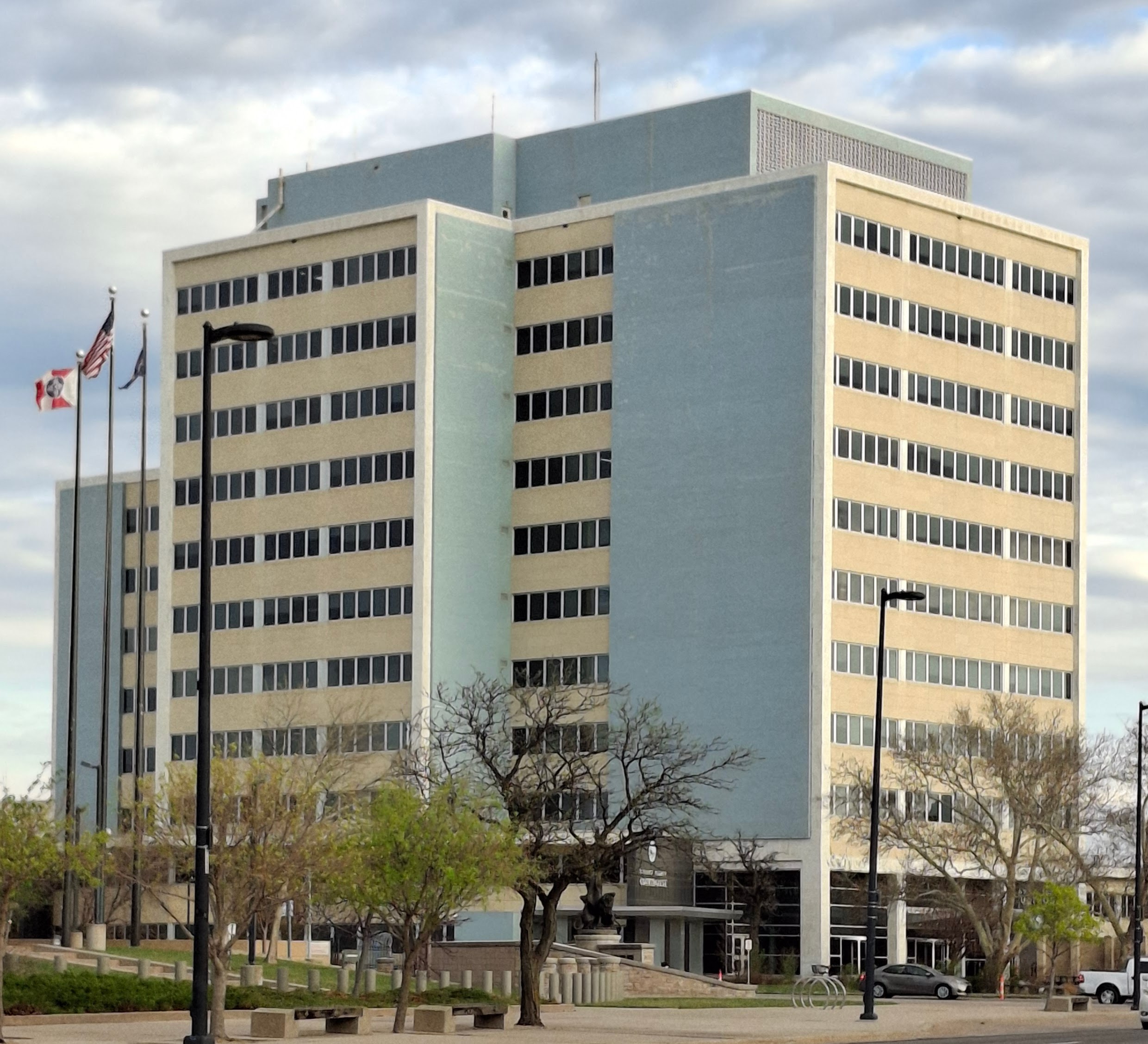 Multi-story government building with flagpoles and bare trees in the foreground.