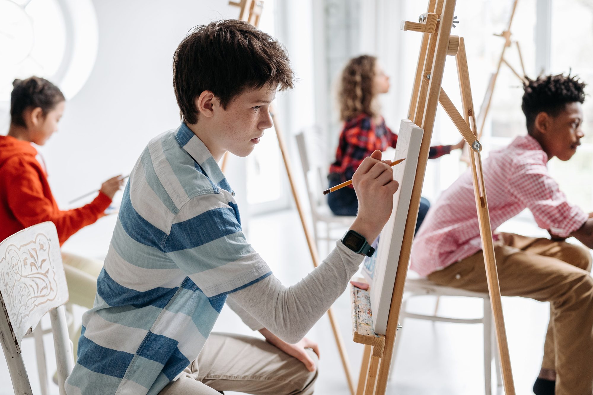 Teens actively participating in an art class indoors, focused on painting and creativity.