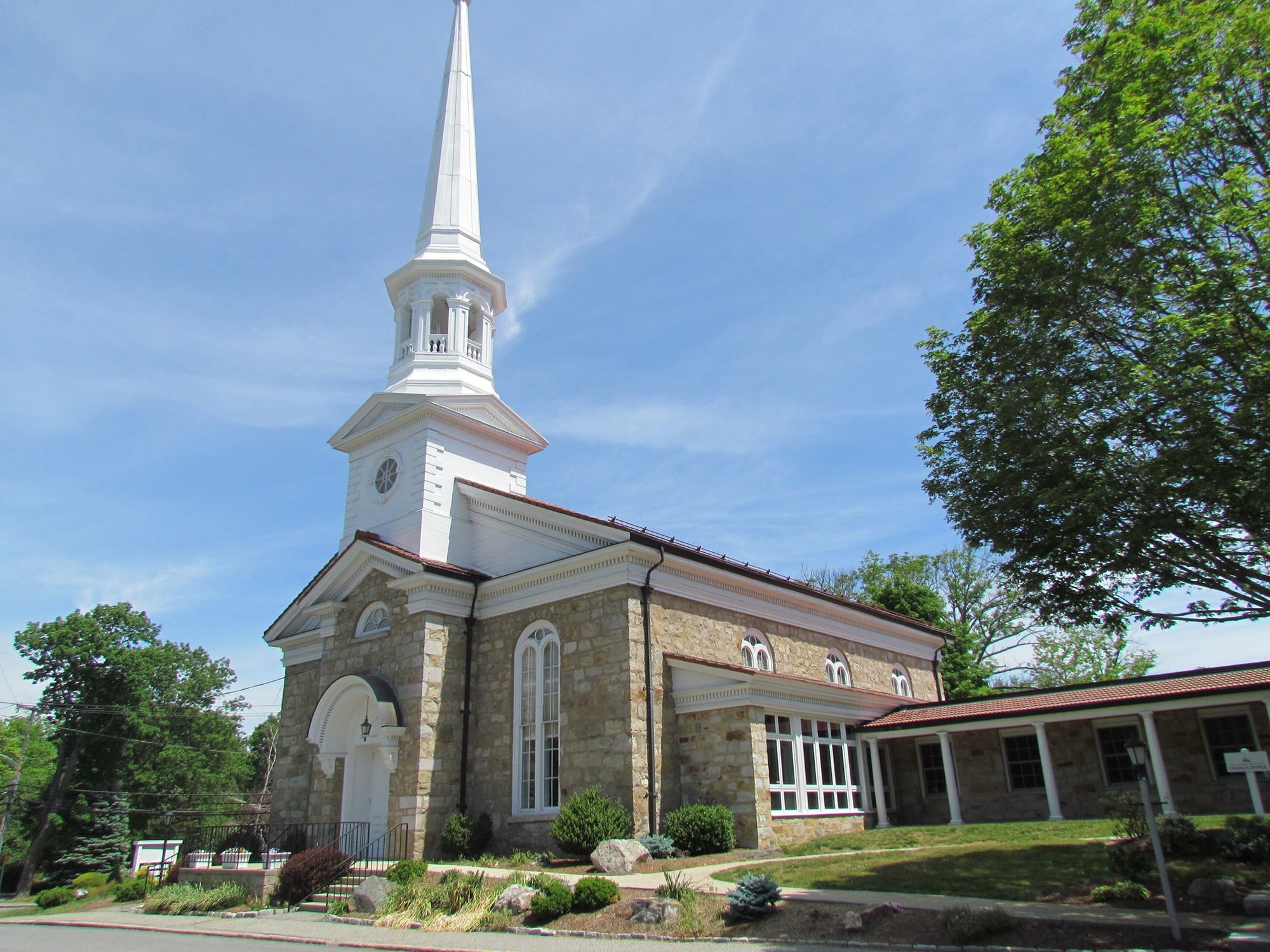 Stone church building with white steeple, arched windows, and a modern addition wing.