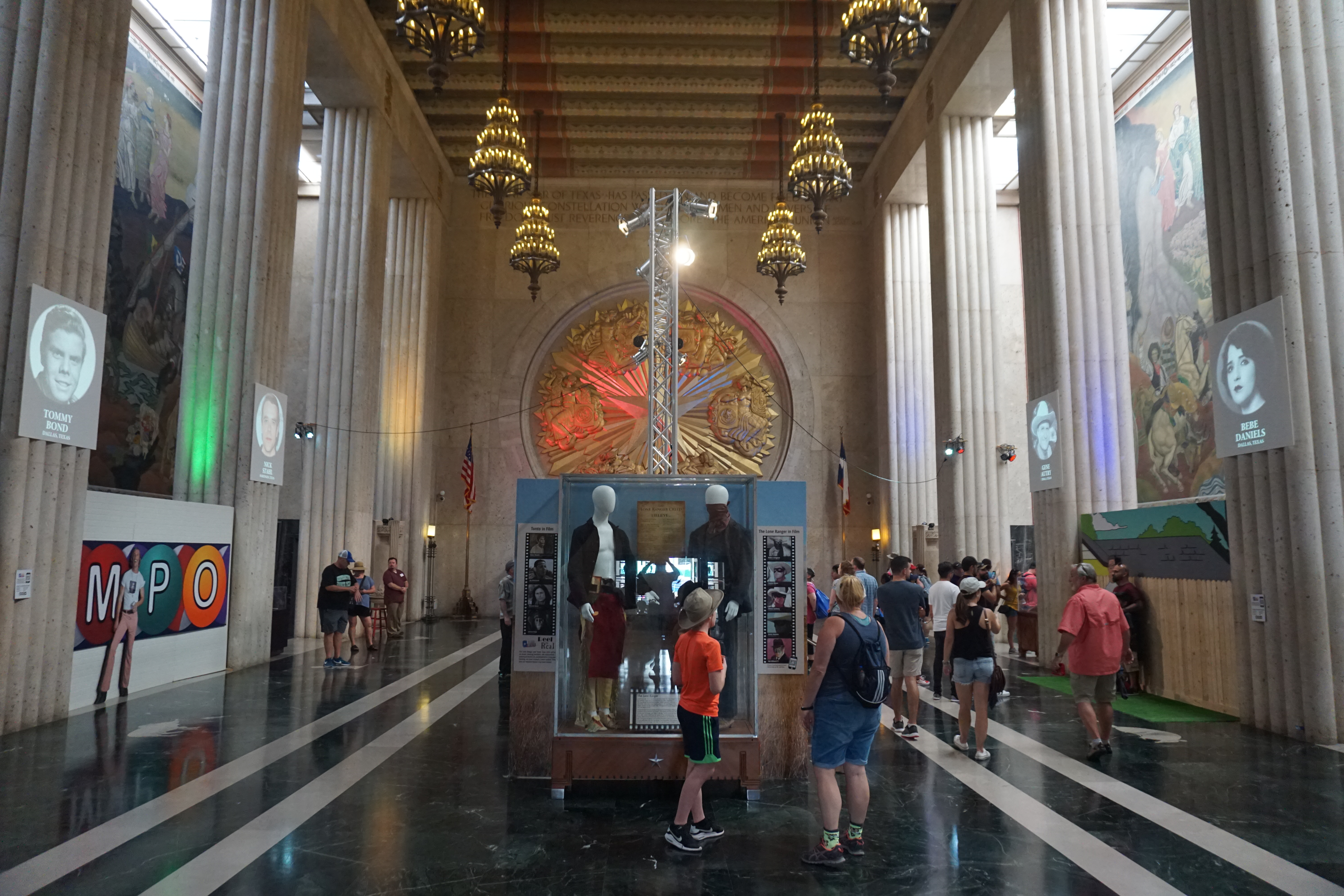 Grand interior hall with tall columns, ornate chandeliers, murals, and display cases