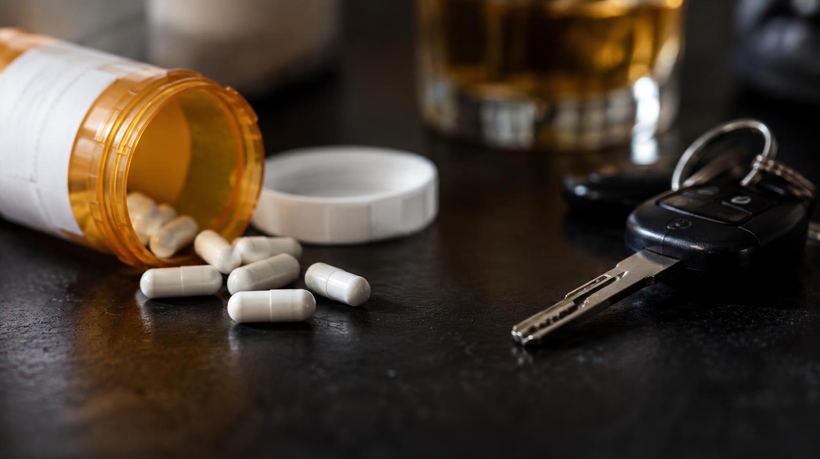 A pill bottle with loose capsules spilled on a dark surface next to car keys.