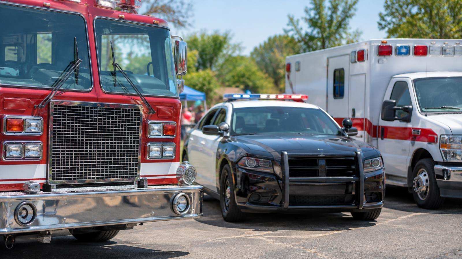 A fire truck, police car, and ambulance parked side by side outdoors on a sunny day.