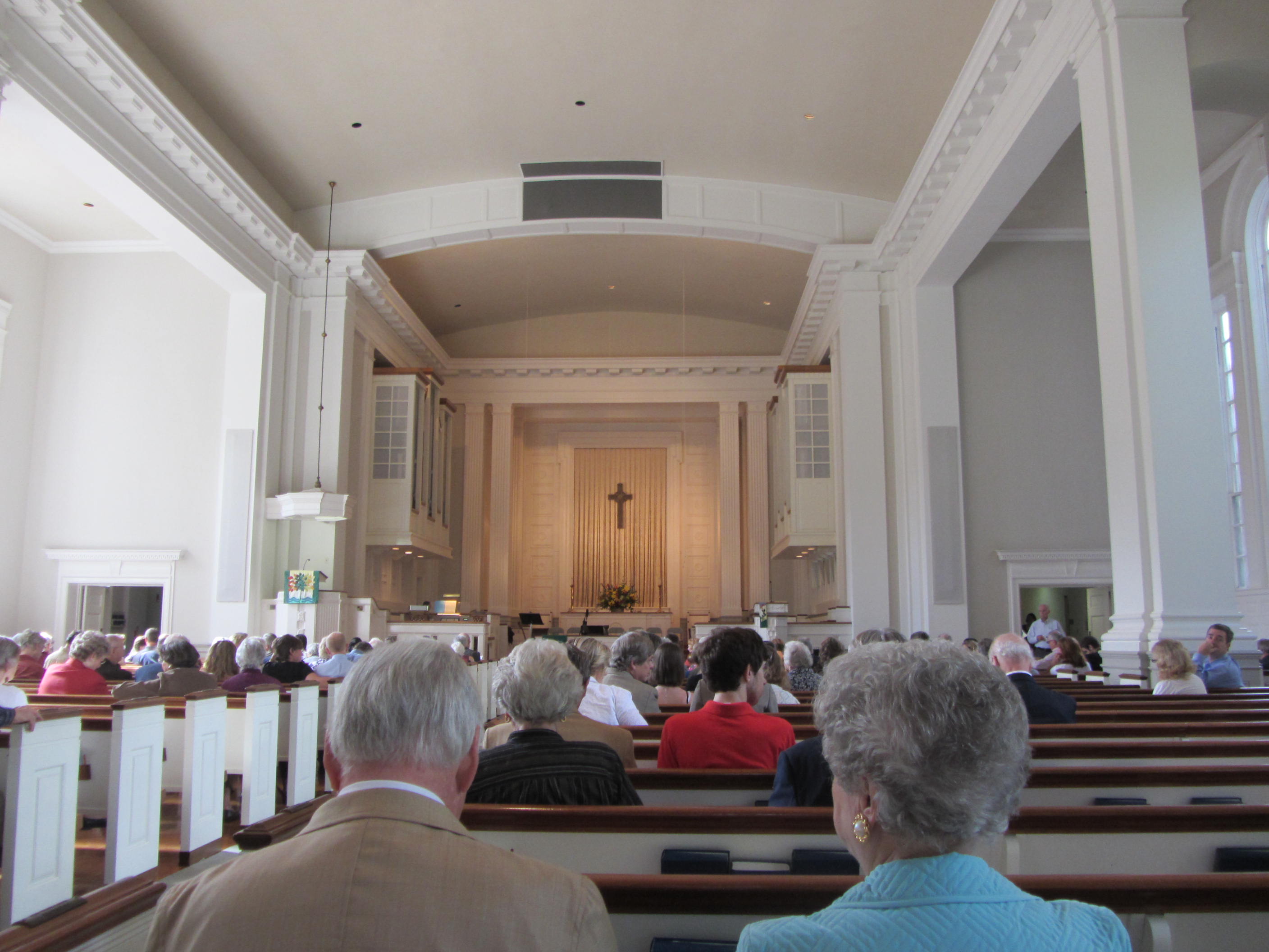 Church sanctuary interior with wooden pews, central aisle, and a cross at the altar.