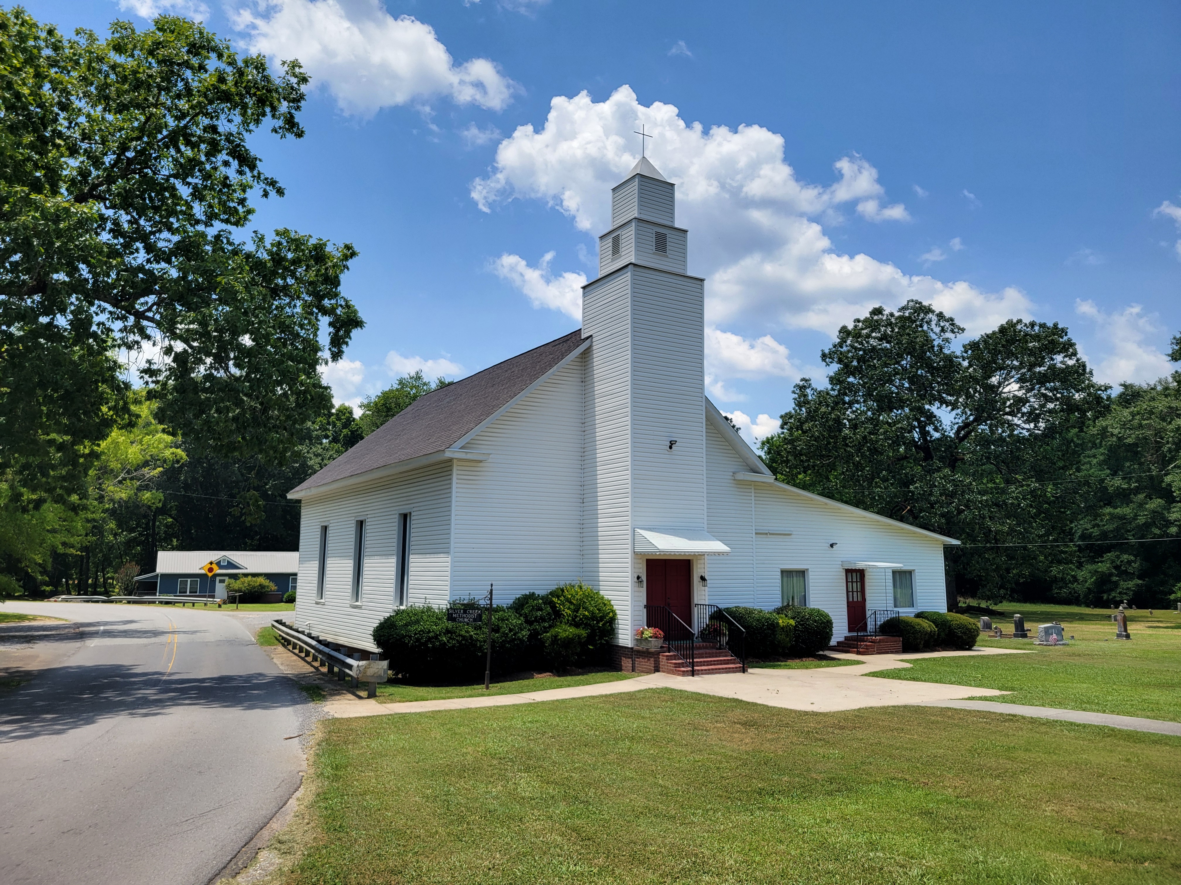 White clapboard church building with square bell tower and red entry doors.