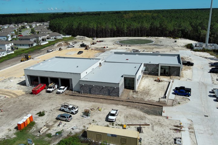 Aerial view of a large flat-roofed public safety building under construction with multiple bay doors.