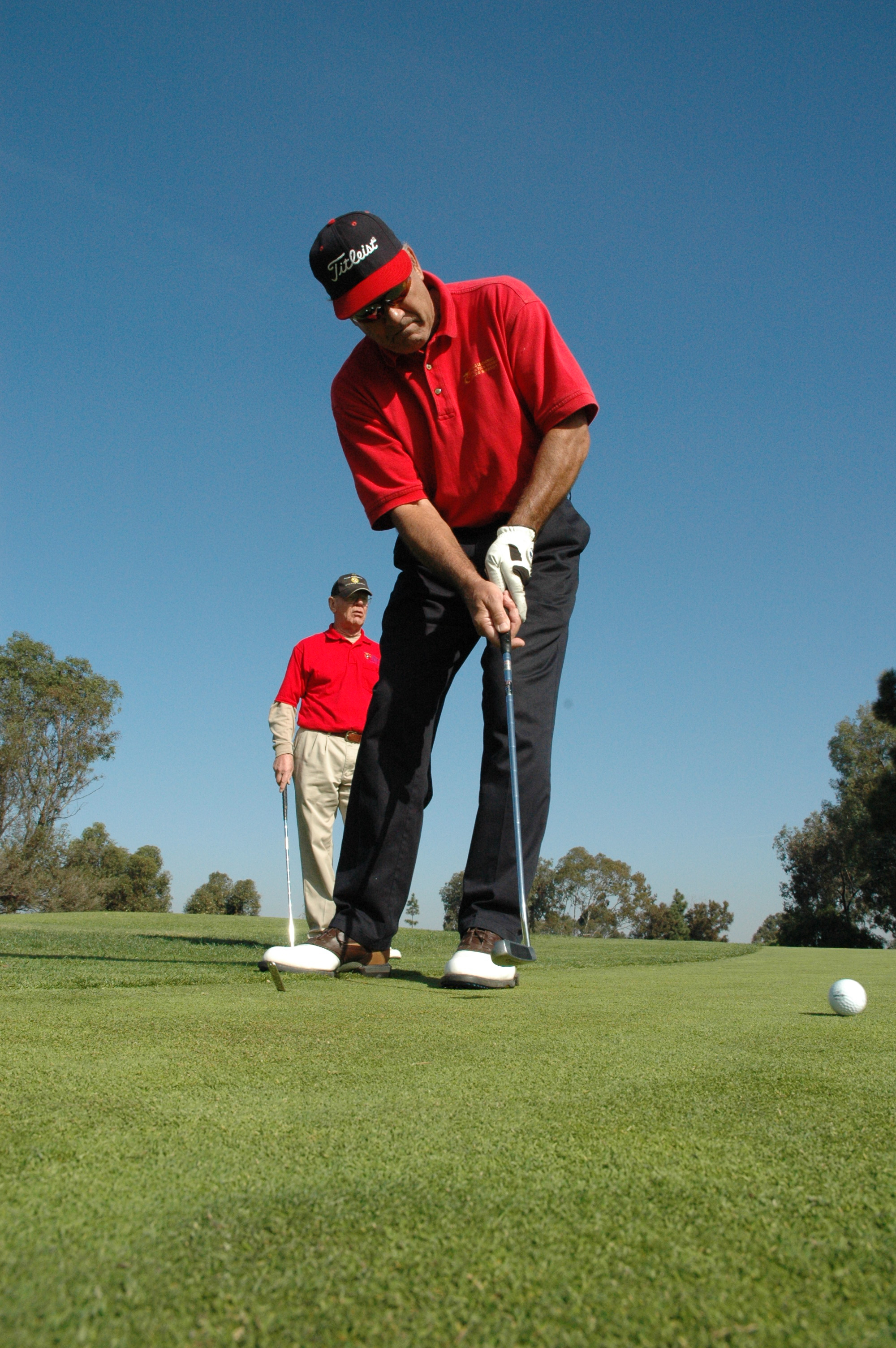 A golfer in a red shirt putts on a green under a clear blue sky.