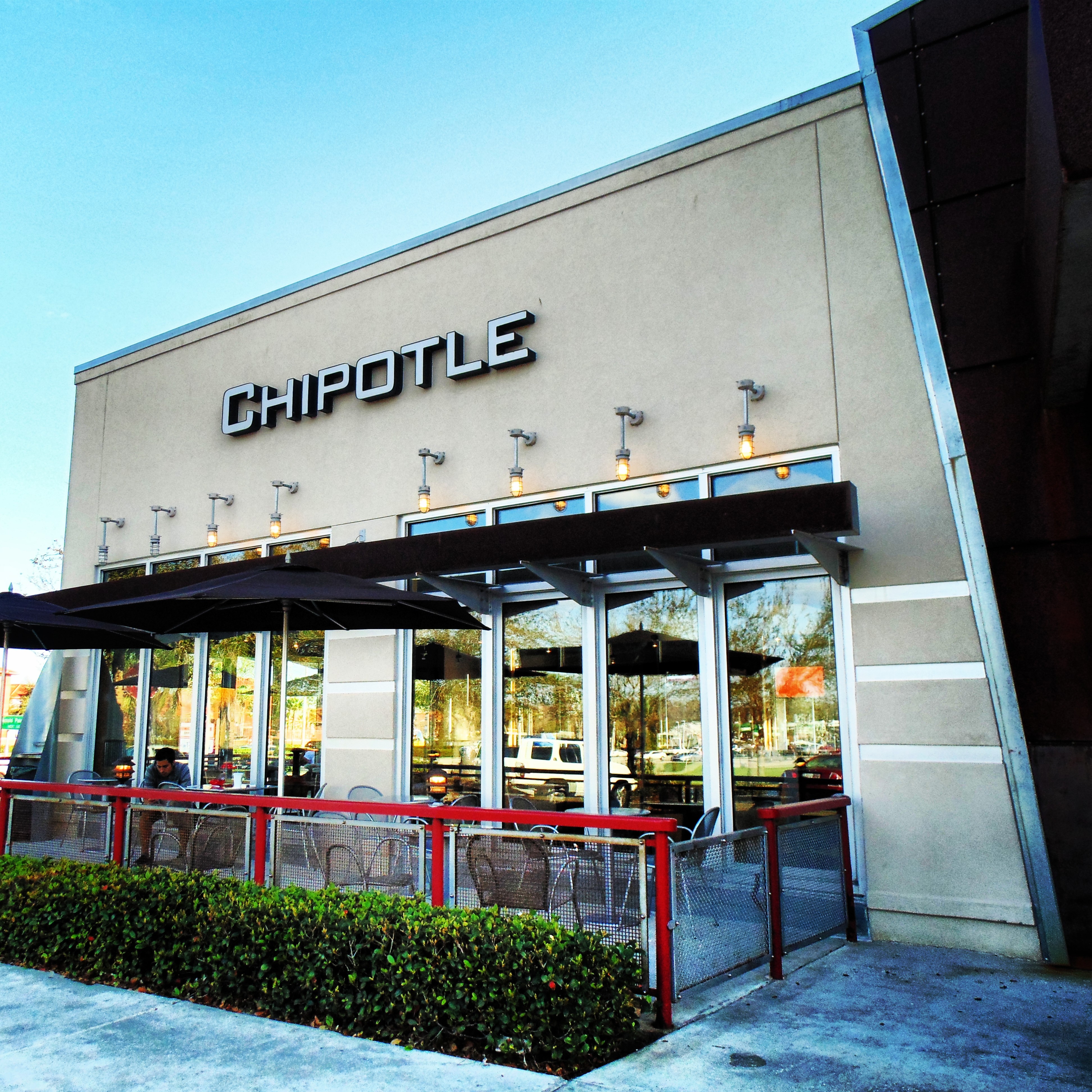 Exterior of a Chipotle Mexican Grill restaurant with outdoor patio seating and umbrellas.