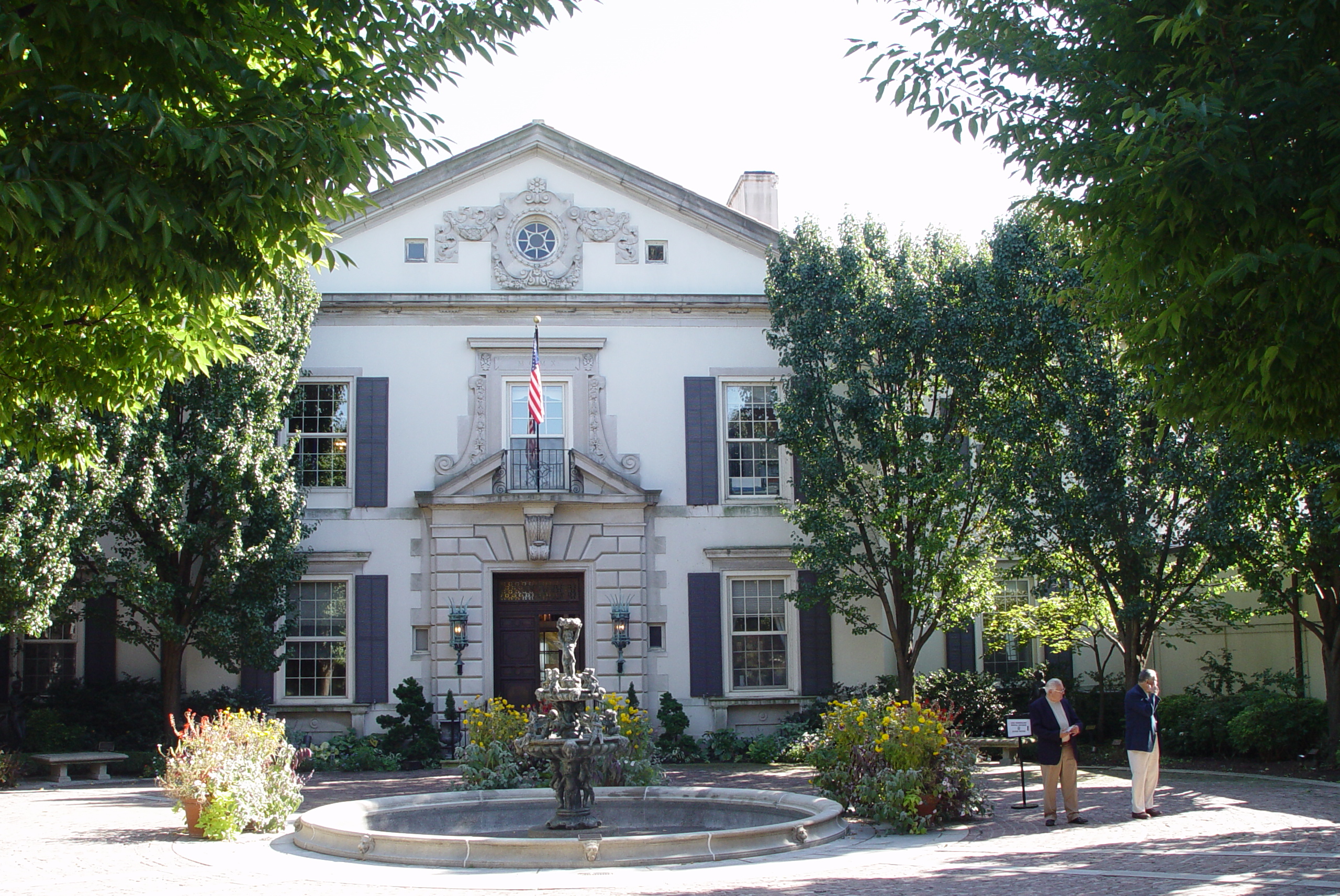White Georgian Colonial mansion with a circular fountain and American flag at the entrance.