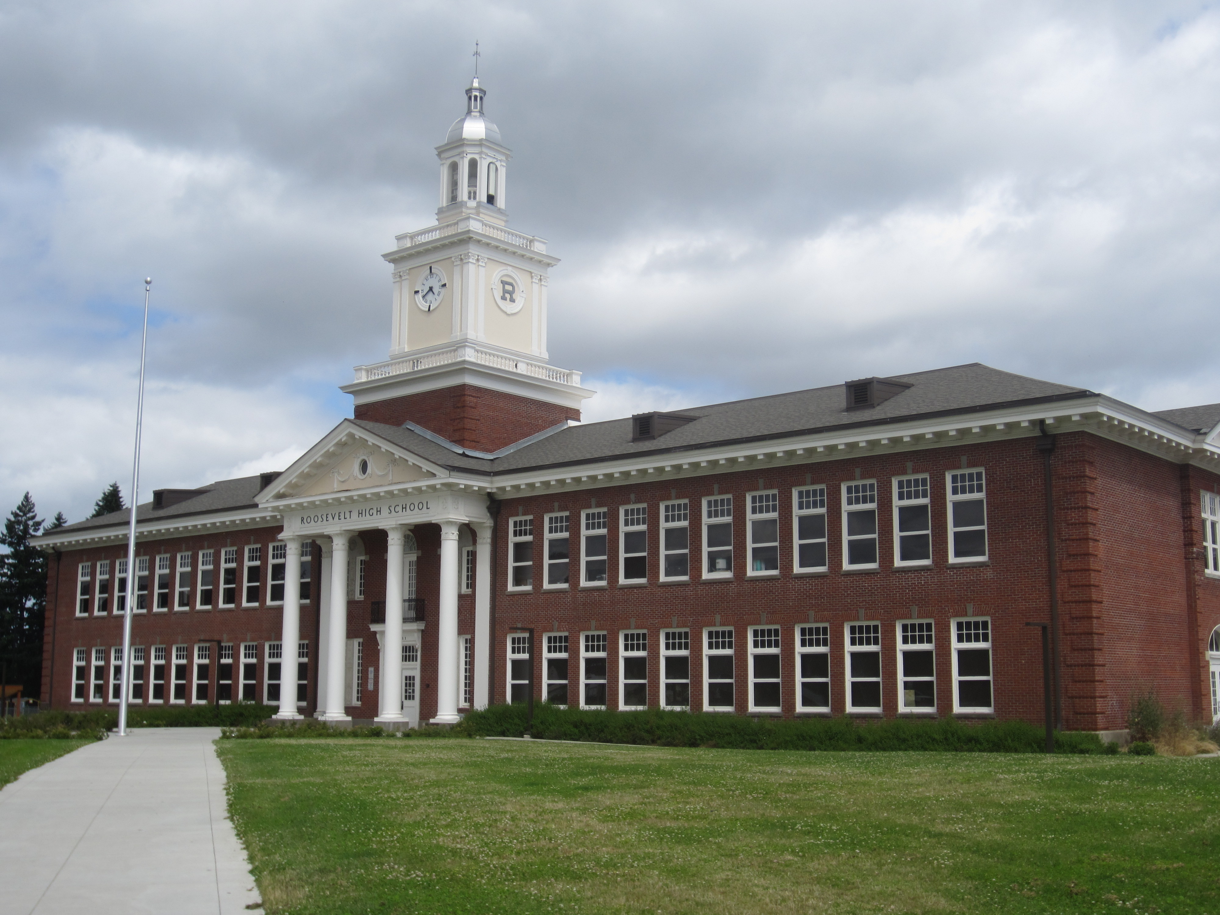Red brick high school building with white clock tower and columned entrance portico.