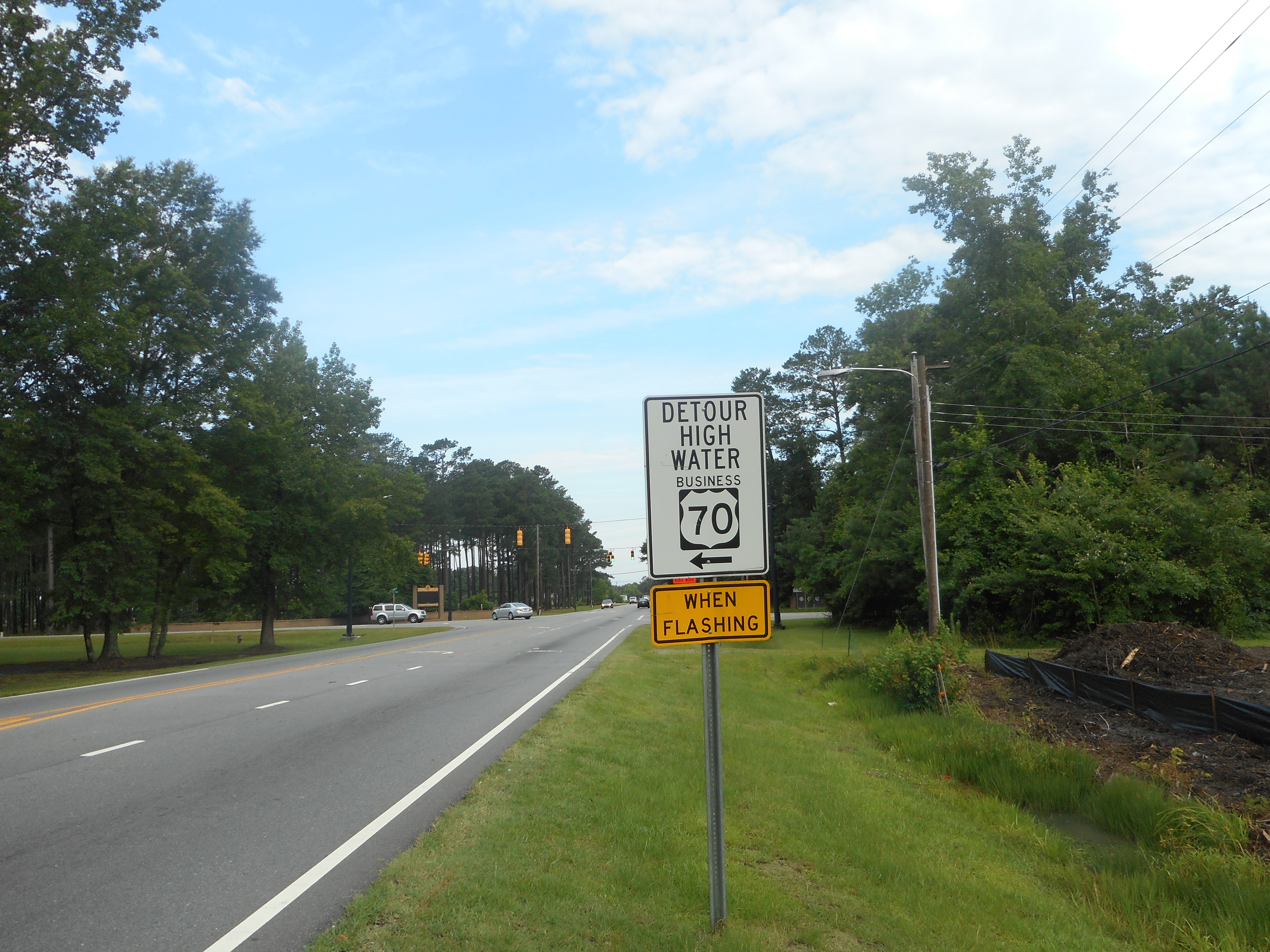 A roadside sign reading 'Detour High Water' with a yellow 'When Flashing' panel on a two-lane highway.