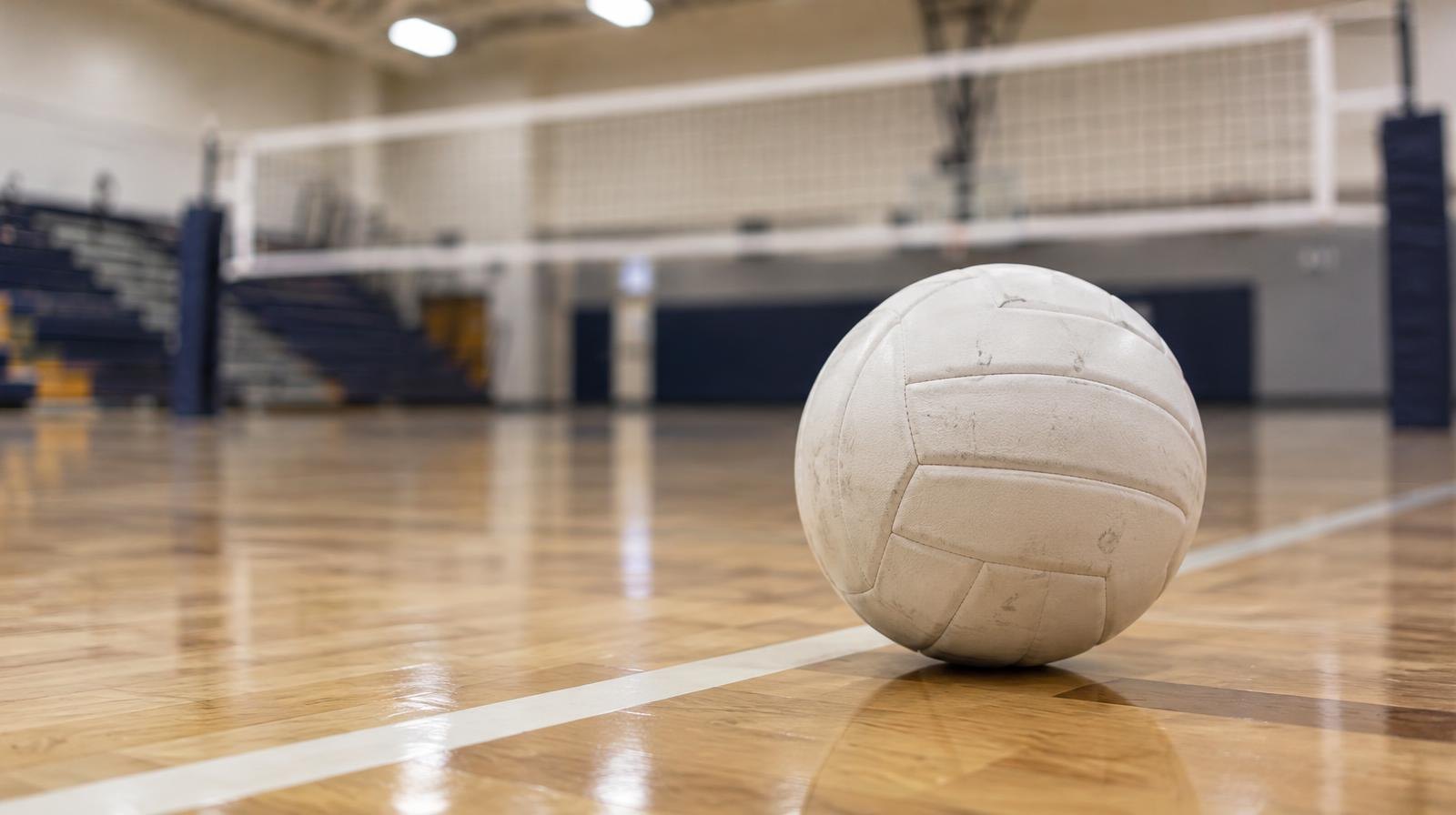 White volleyball resting on a hardwood gym floor near a painted boundary line.