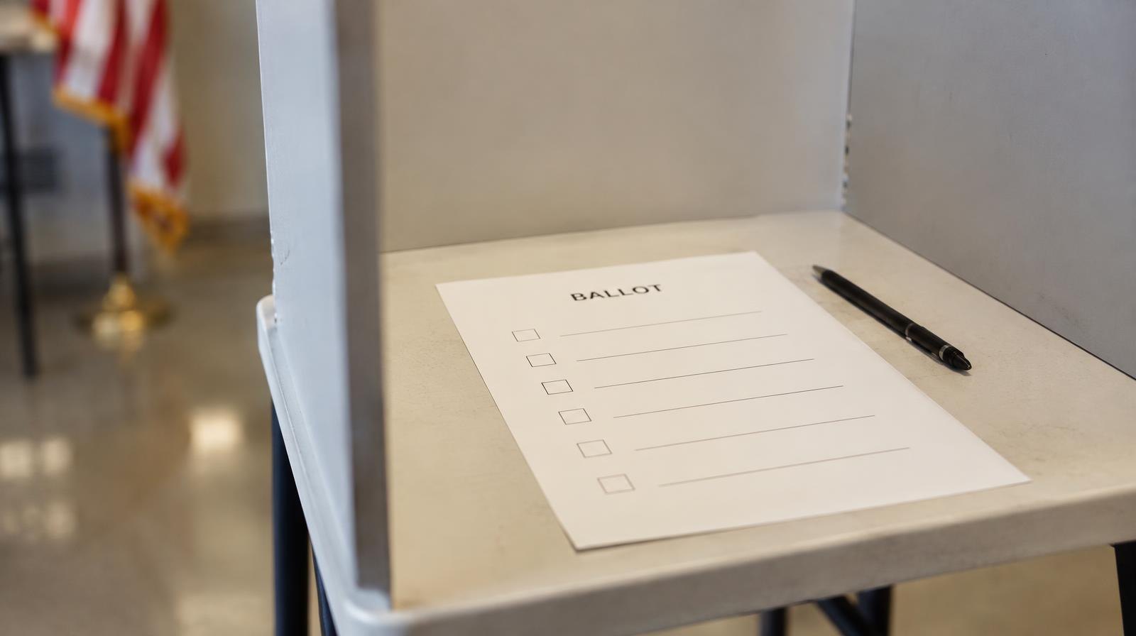 A blank paper ballot rests inside a voting booth beside a black pen.