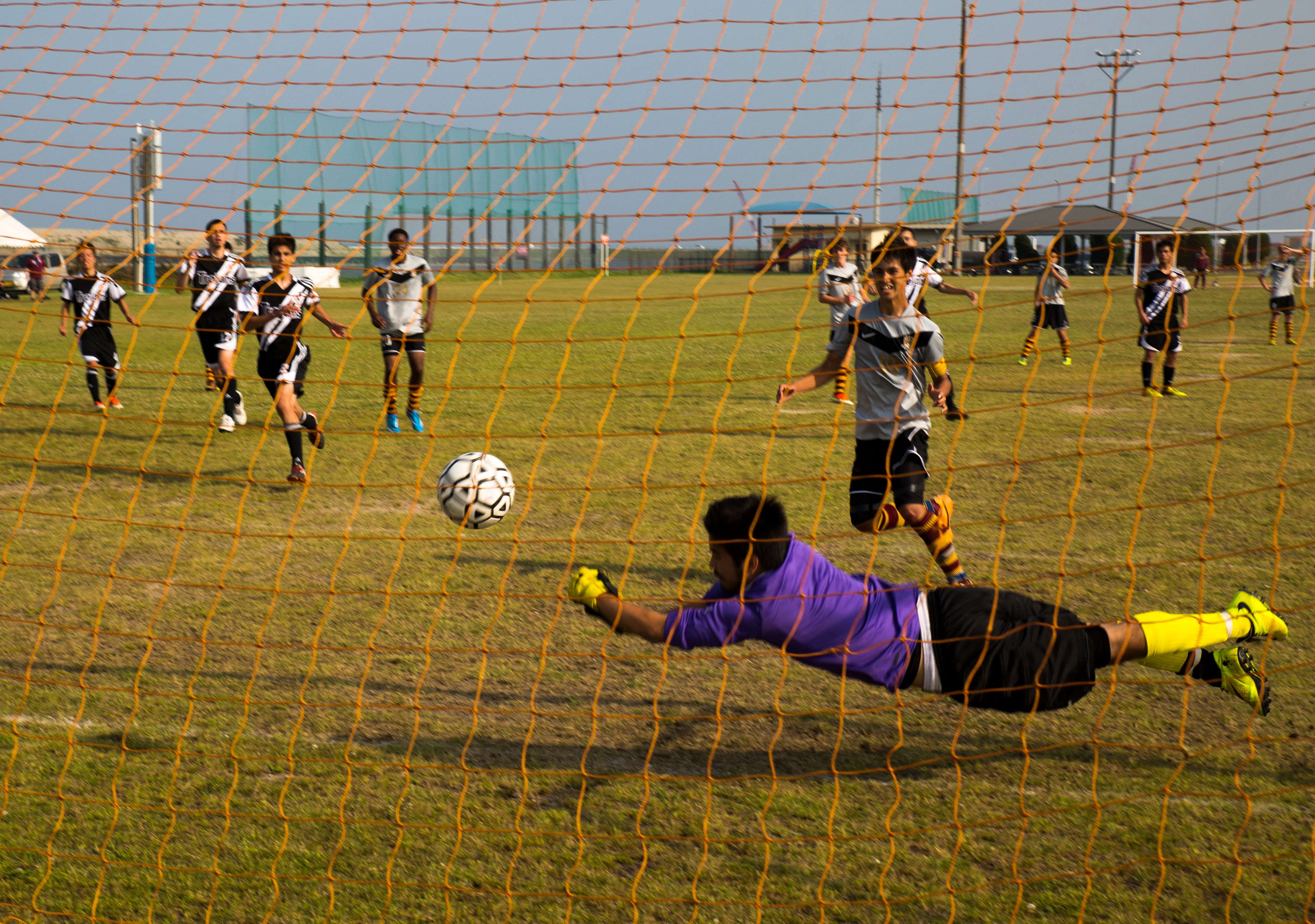A goalkeeper in a purple uniform dives to his right to stop a soccer ball.