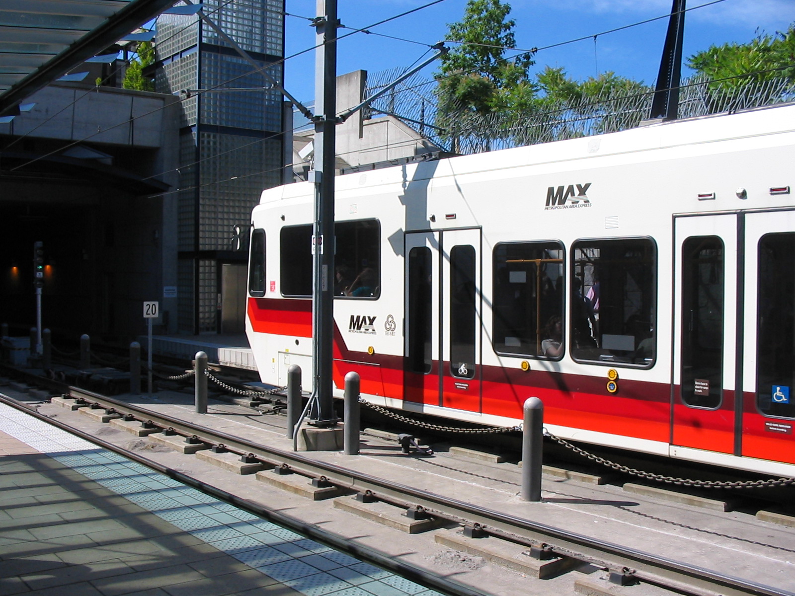 A MAX light rail train stopped at a covered station platform with overhead electric wires.