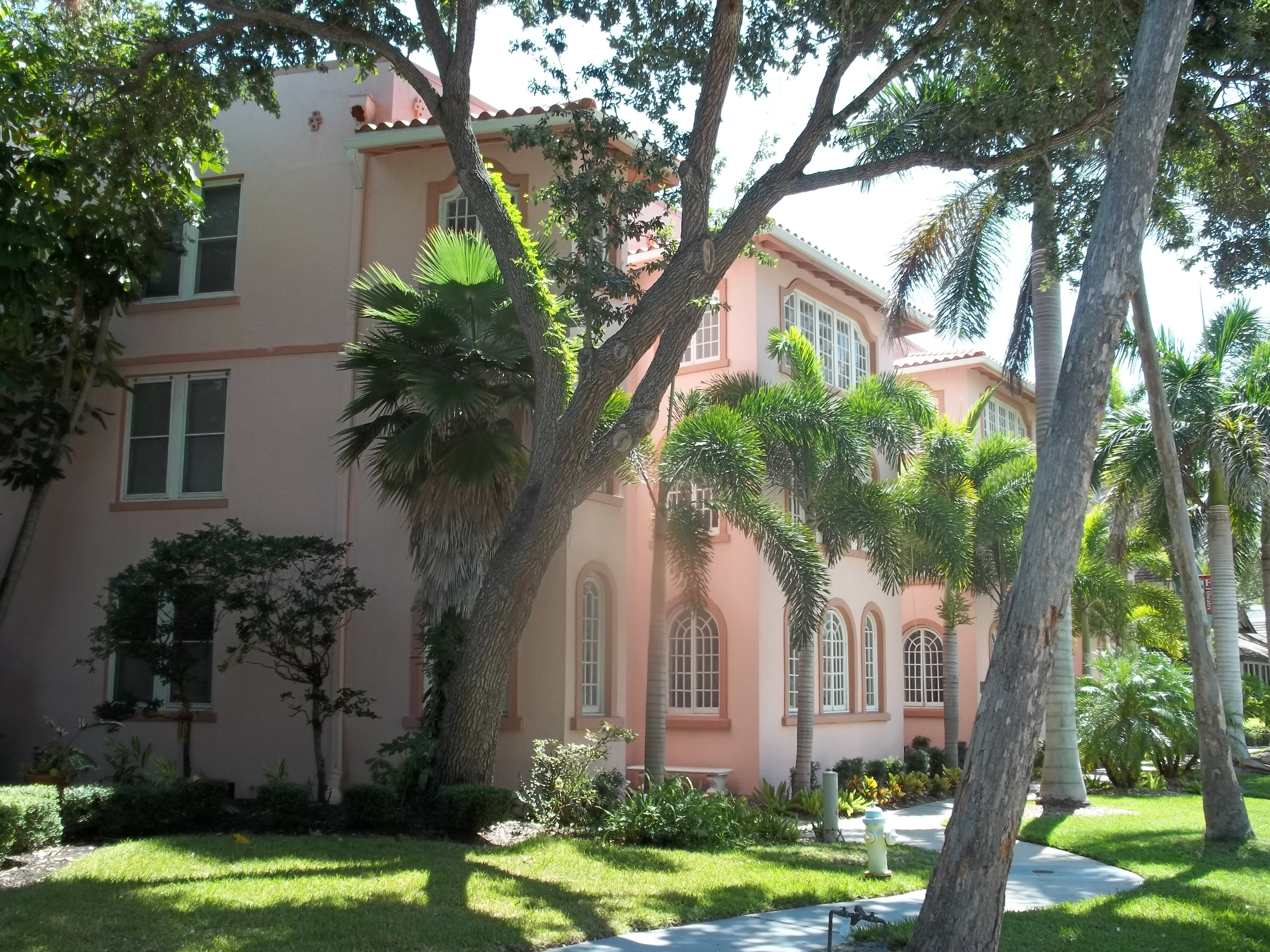 Pink stucco two-story apartment building with palm trees on a sunny day.