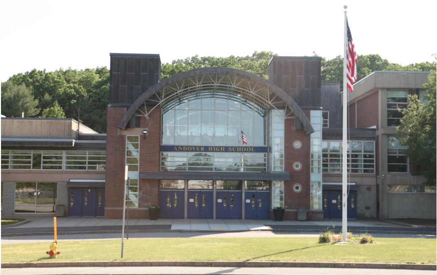 Brick school building with large arched glass entrance and American flag on flagpole.