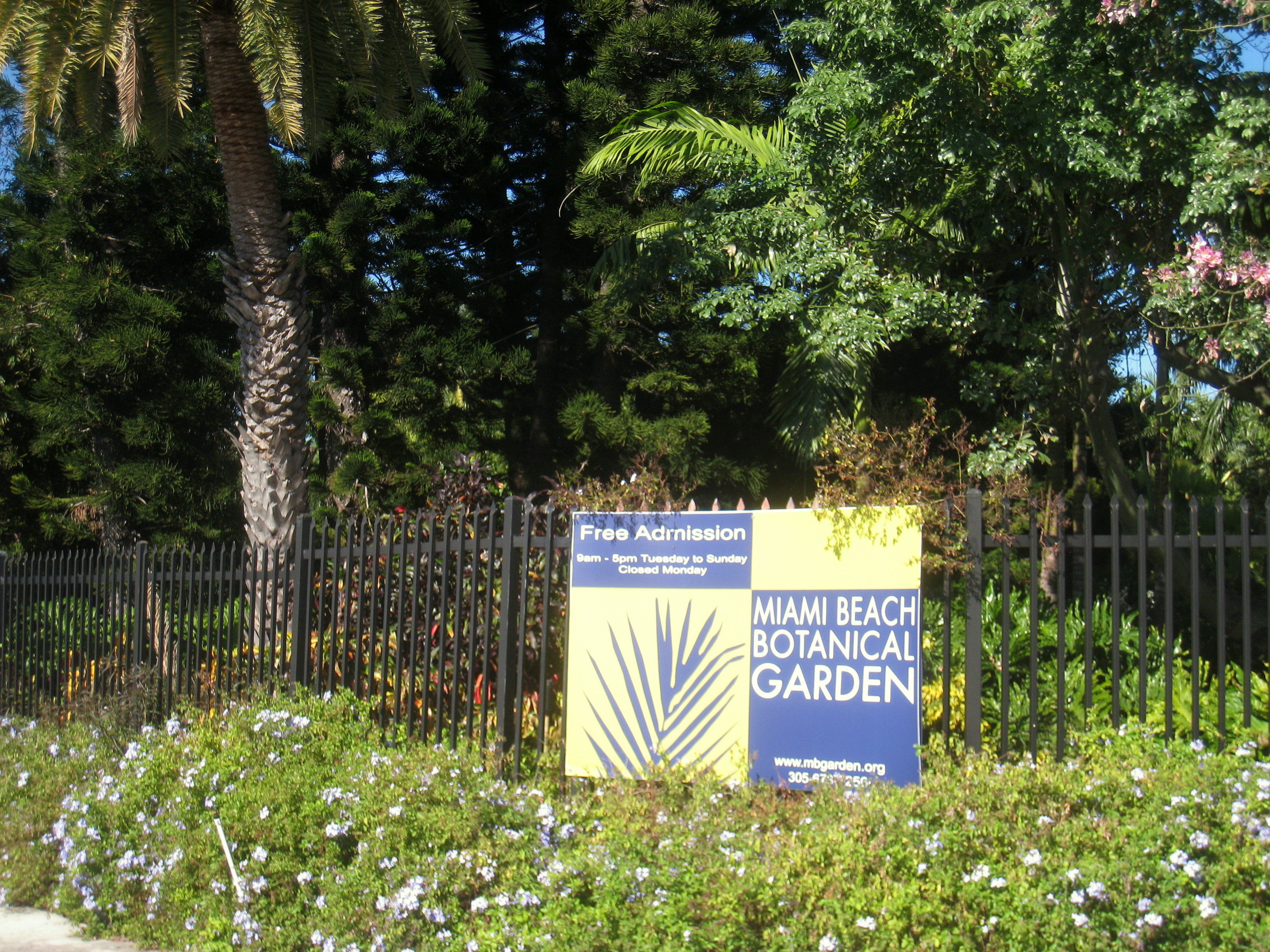 Sign for Miami Beach Botanical Garden with free admission notice beside a black iron fence.