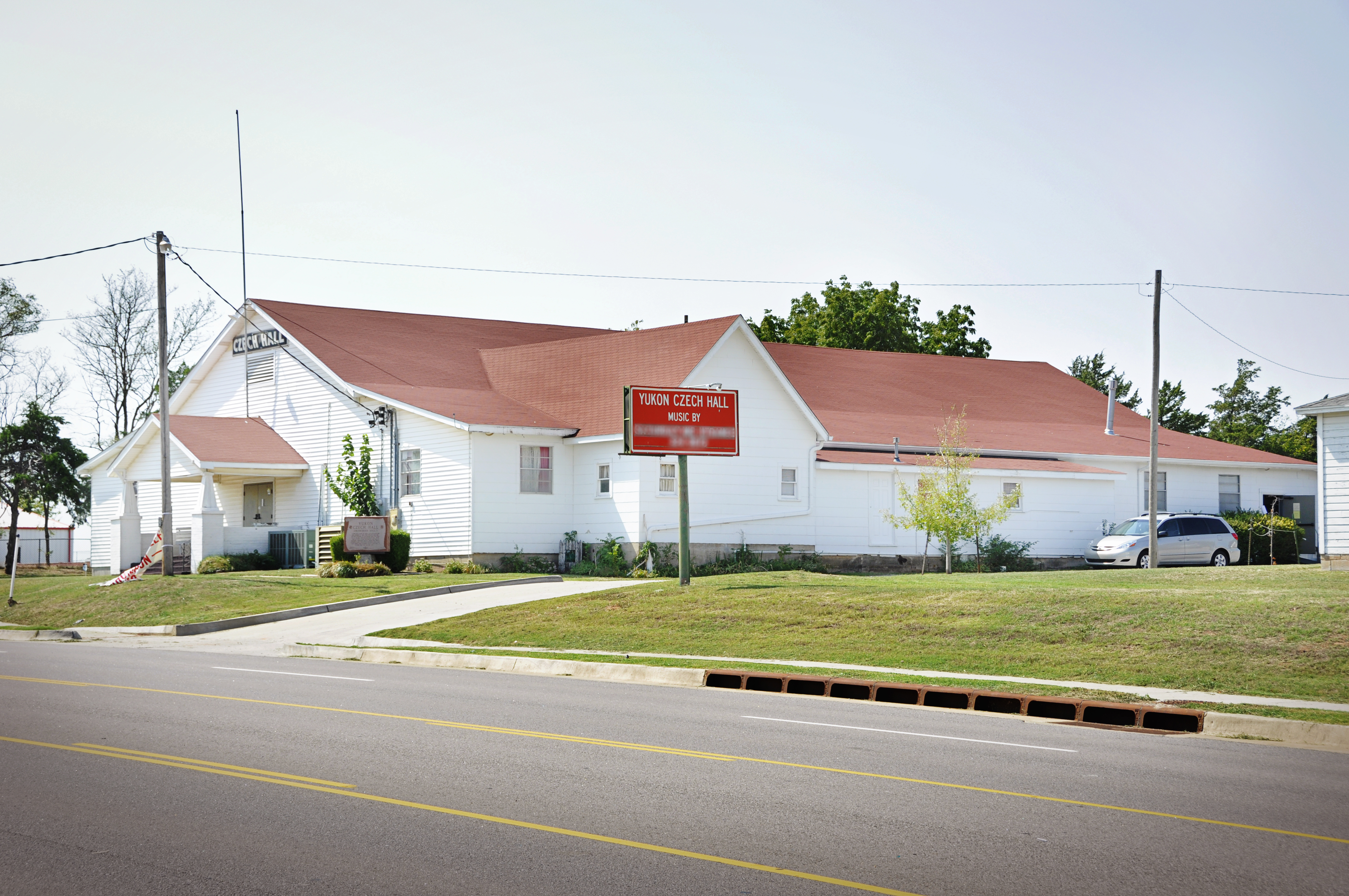 White single-story building with a red metal roof and red sign on a corner lot.