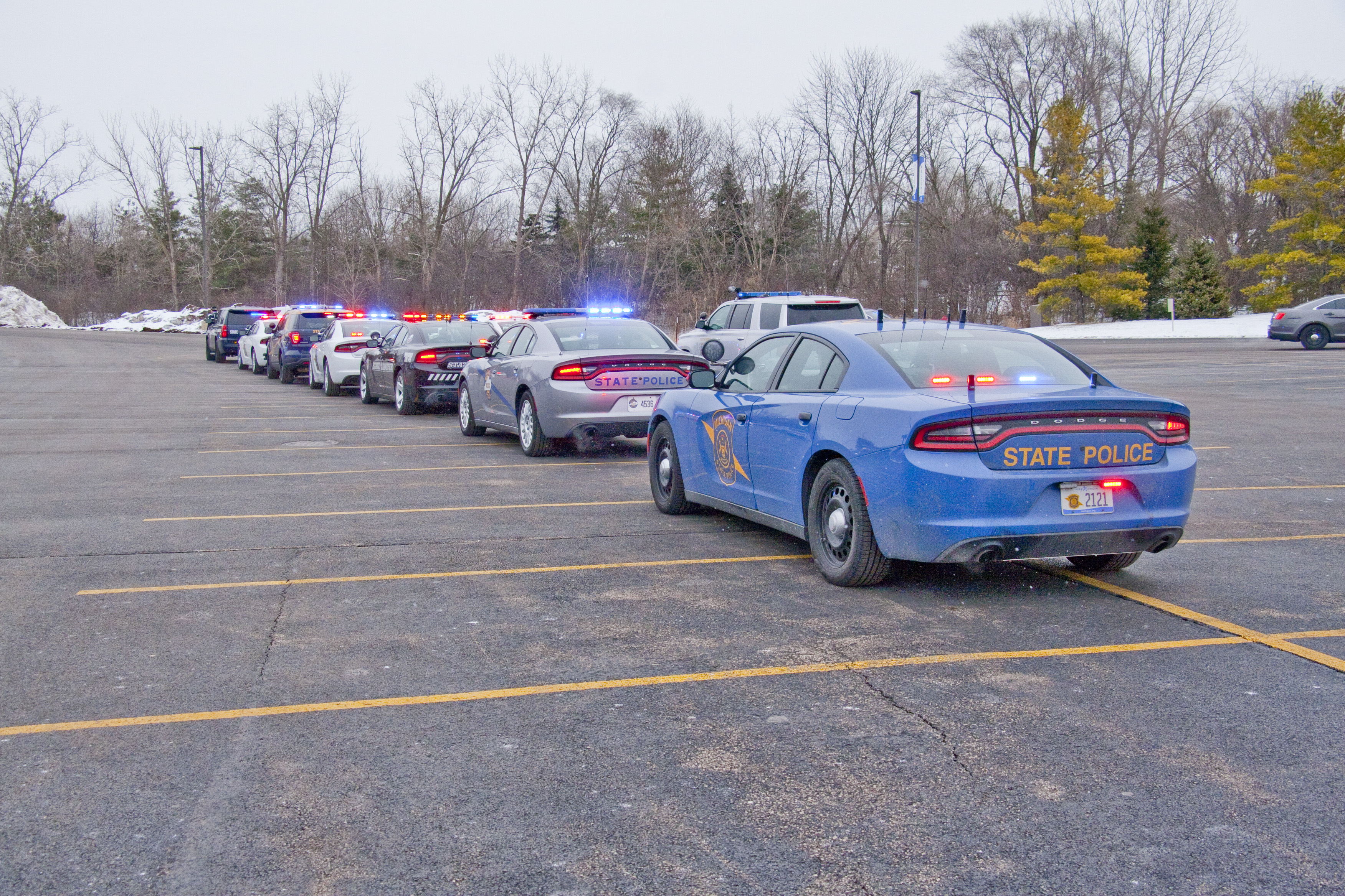 A row of Michigan State Police patrol cars with blue emergency lights activated.