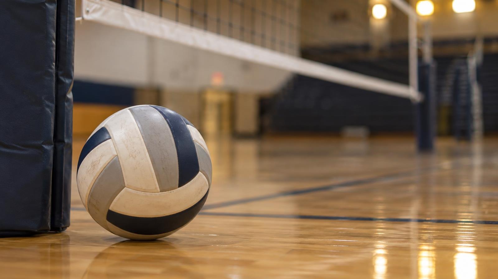 A volleyball resting on a hardwood gymnasium floor beside the net post.