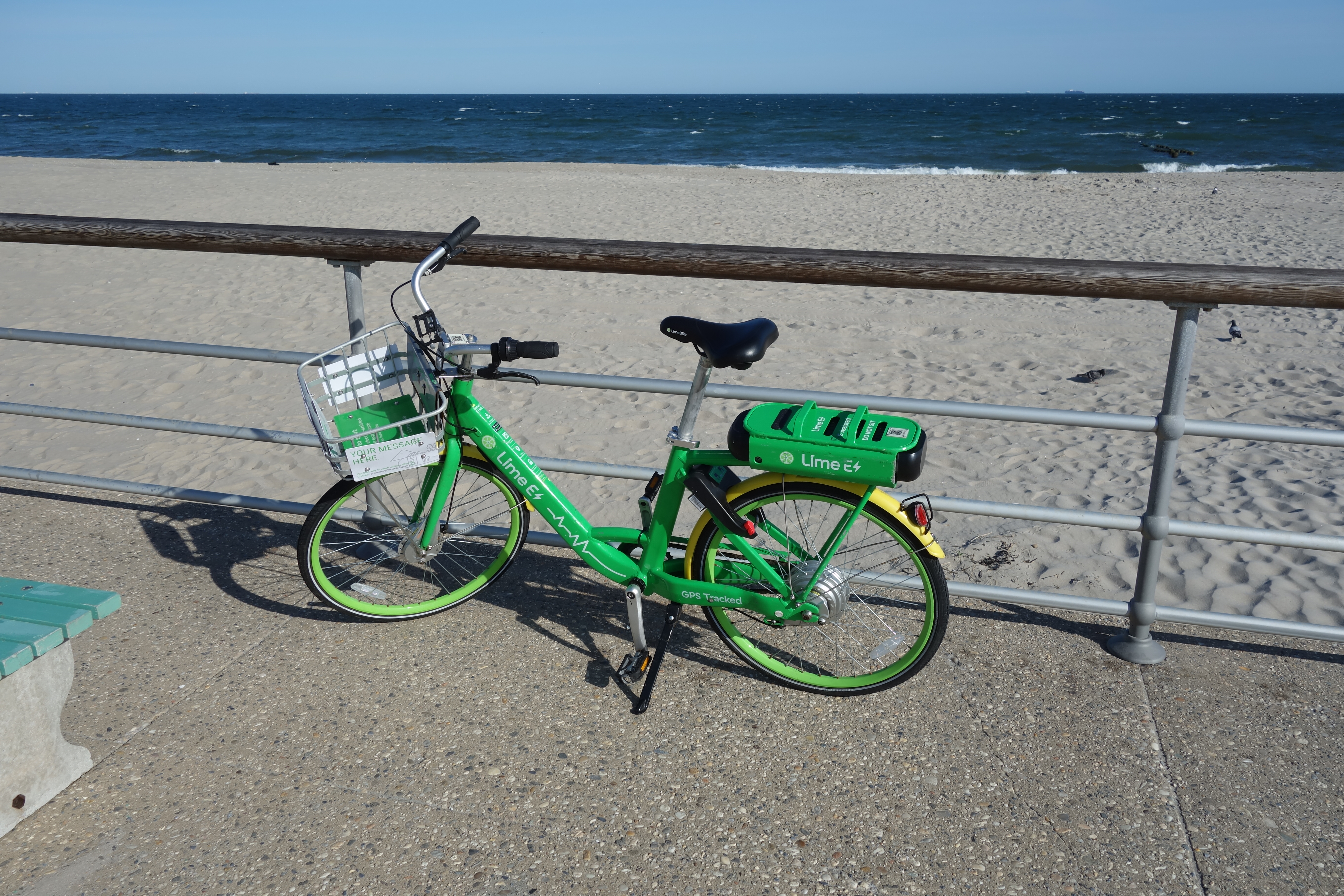 A green Lime e-bike leaned against a metal railing on a boardwalk near a beach.