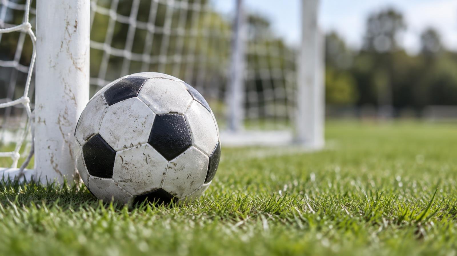 A black-and-white soccer ball on green grass beside a white goal net.