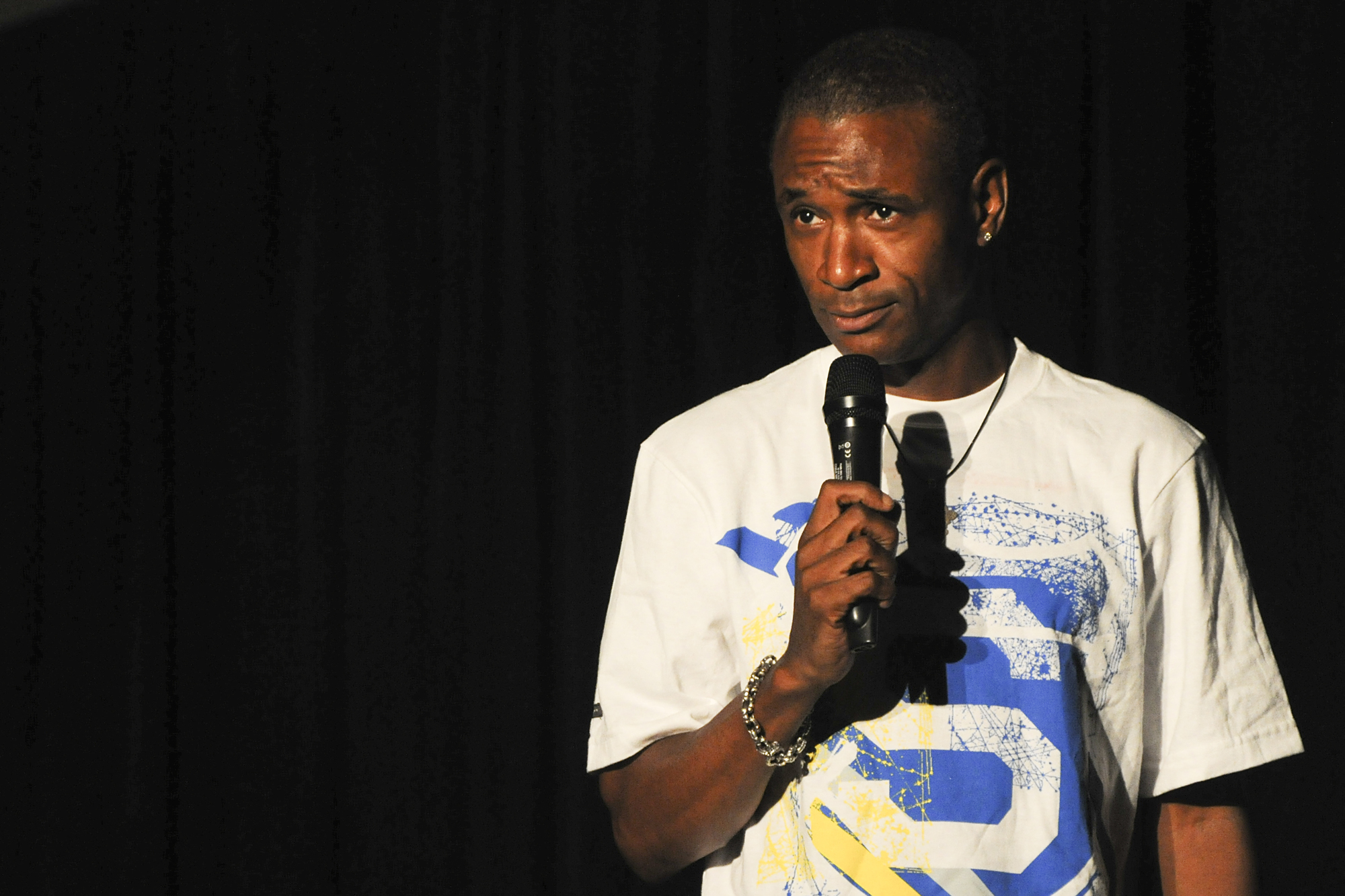Comedian holding a microphone on a darkened stage performing stand-up.