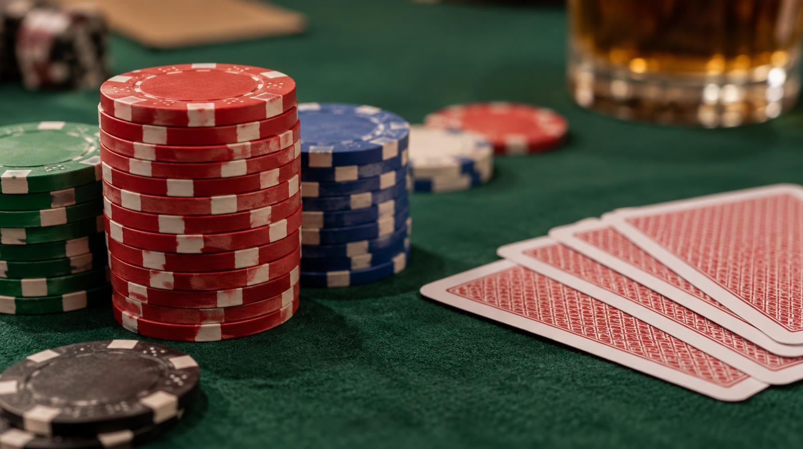 Stack of colorful poker chips beside face-down playing cards on green felt.
