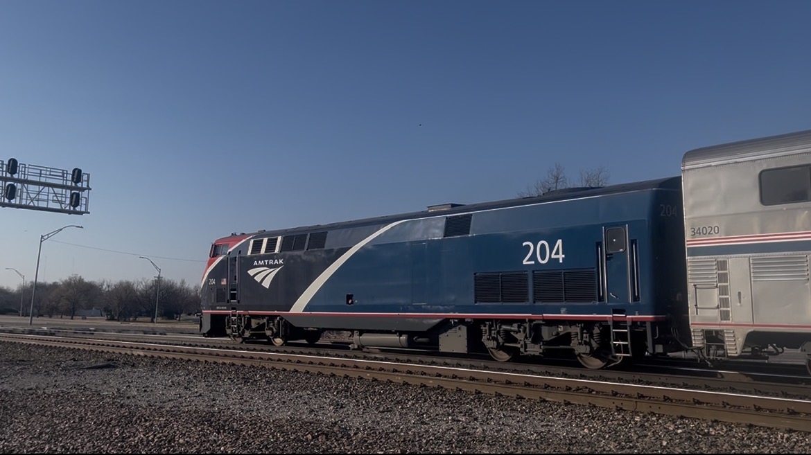 Amtrak locomotive pulling silver passenger cars on a rail line under a blue sky.