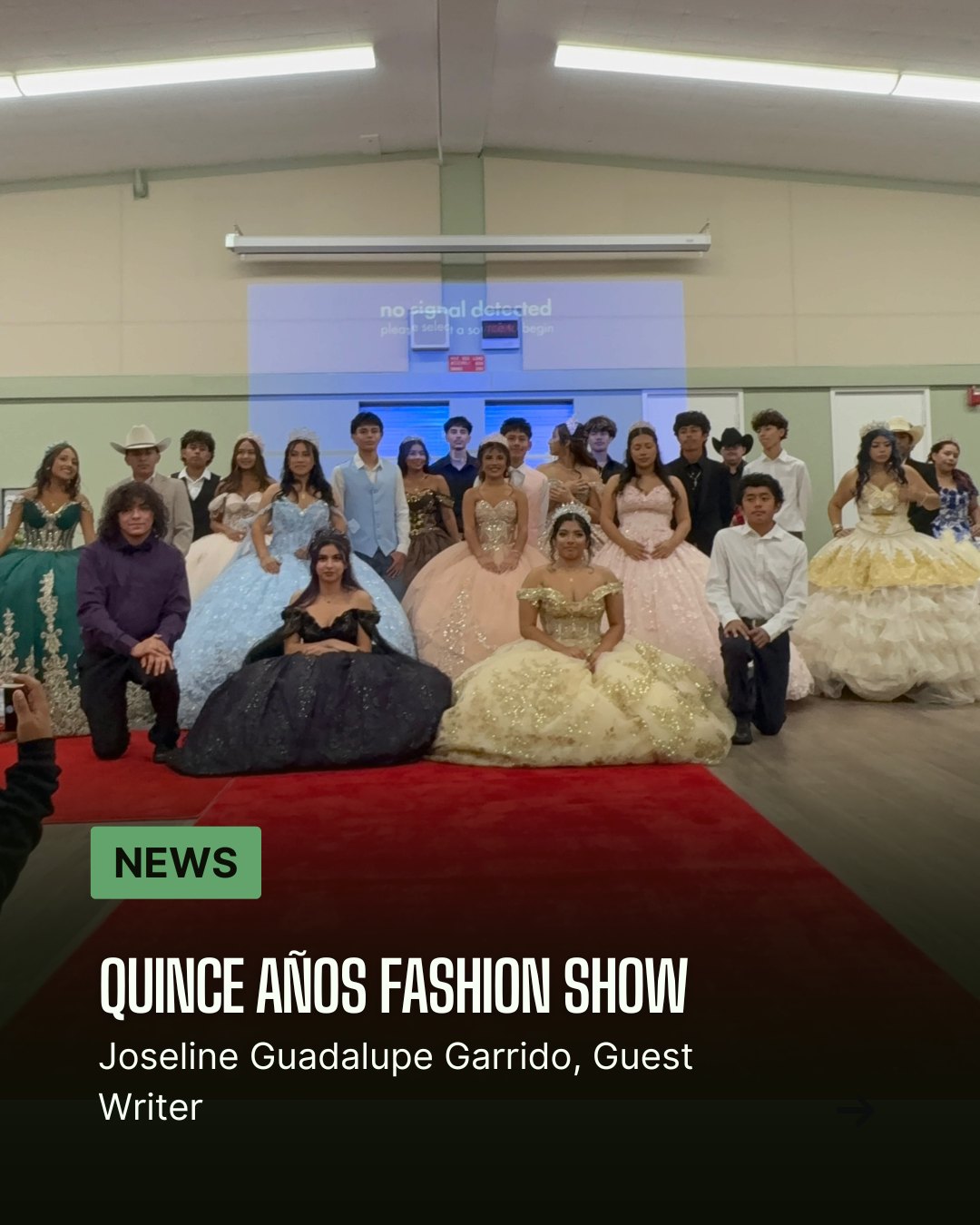 Students in colorful ballgowns and suits posed on a red carpet indoors.