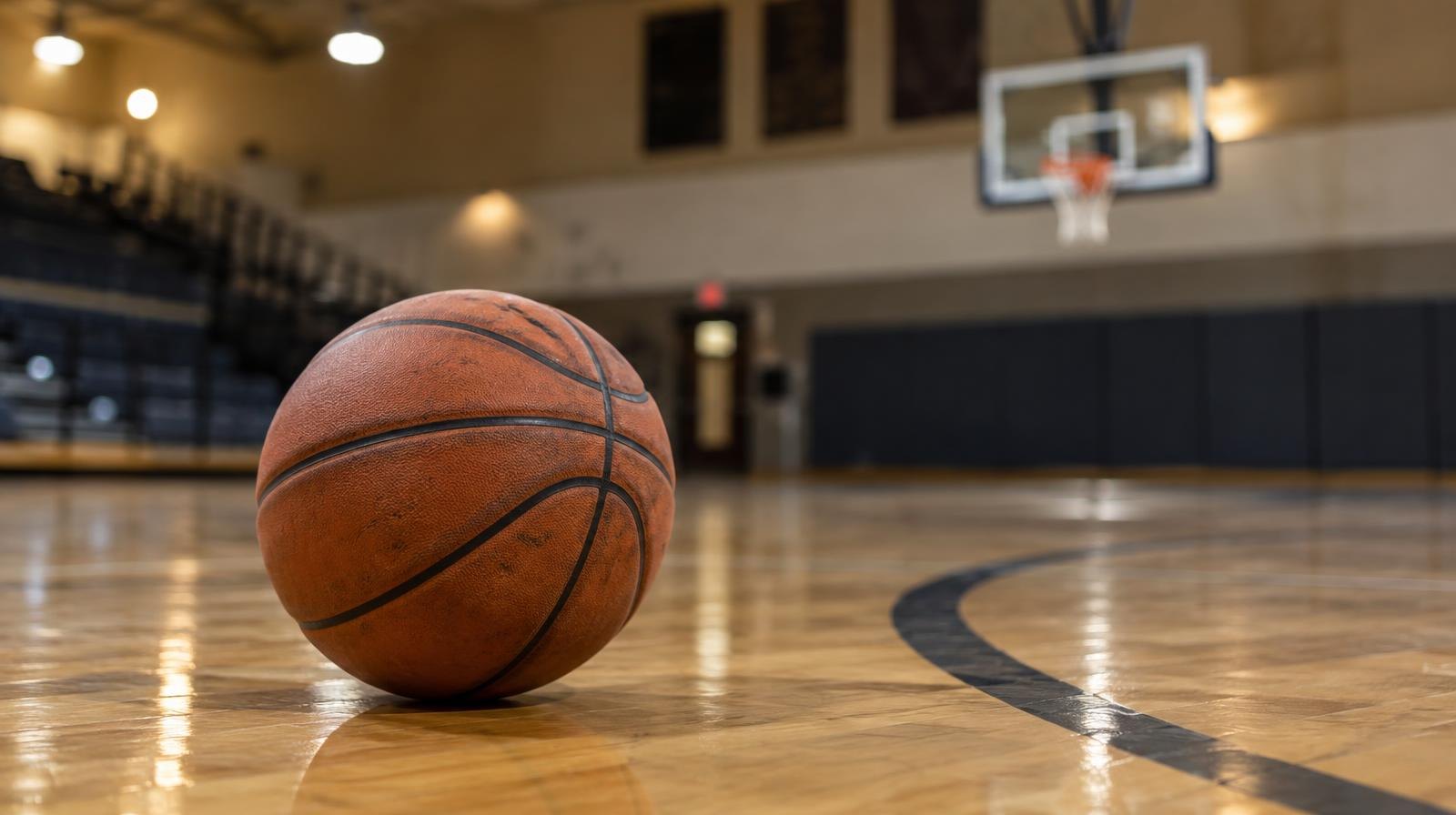 A basketball resting on a hardwood gym floor near the three-point arc.