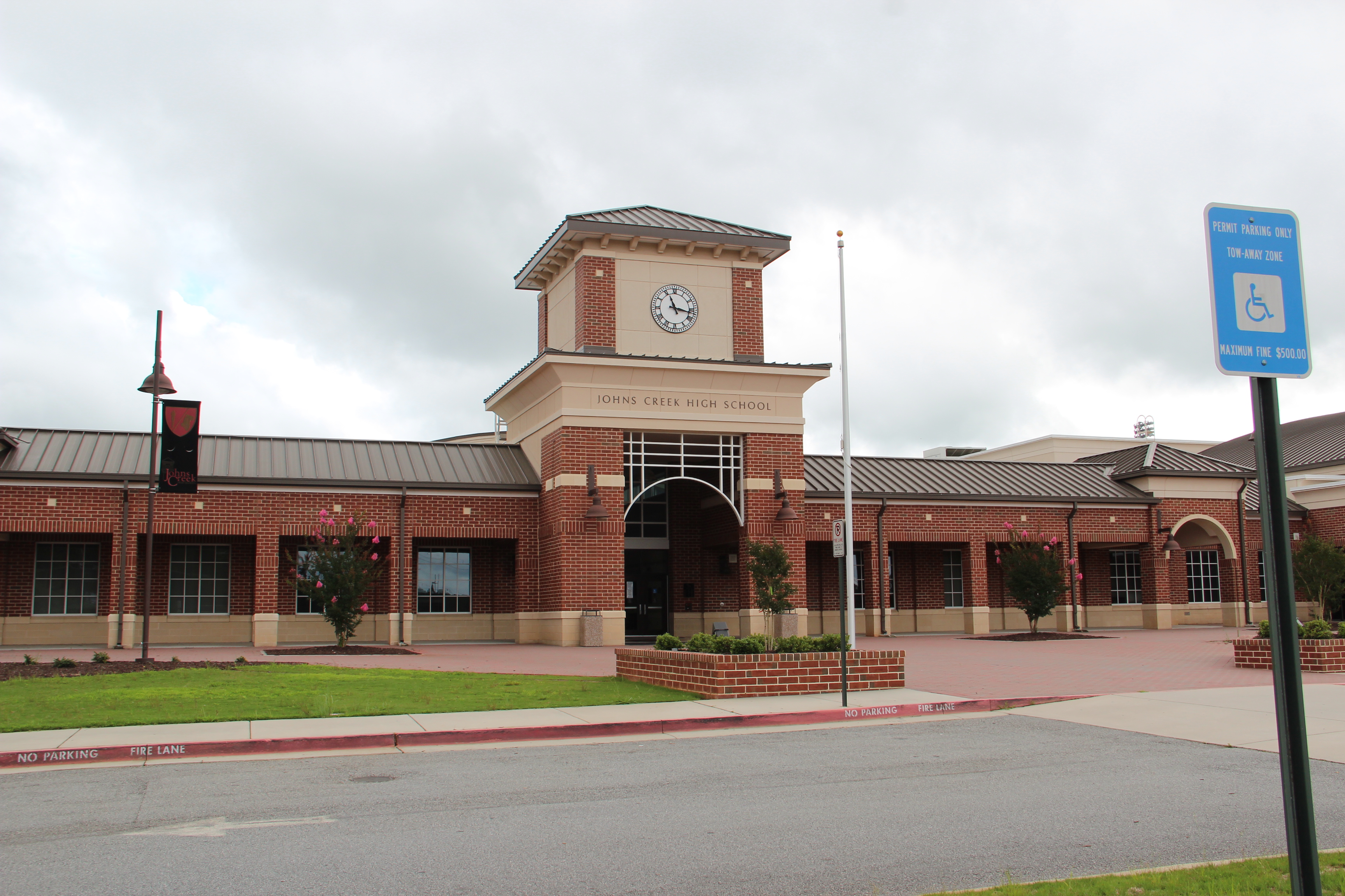 Exterior of a brick school building with clock tower, arched entrance, and flagpole under overcast sky.