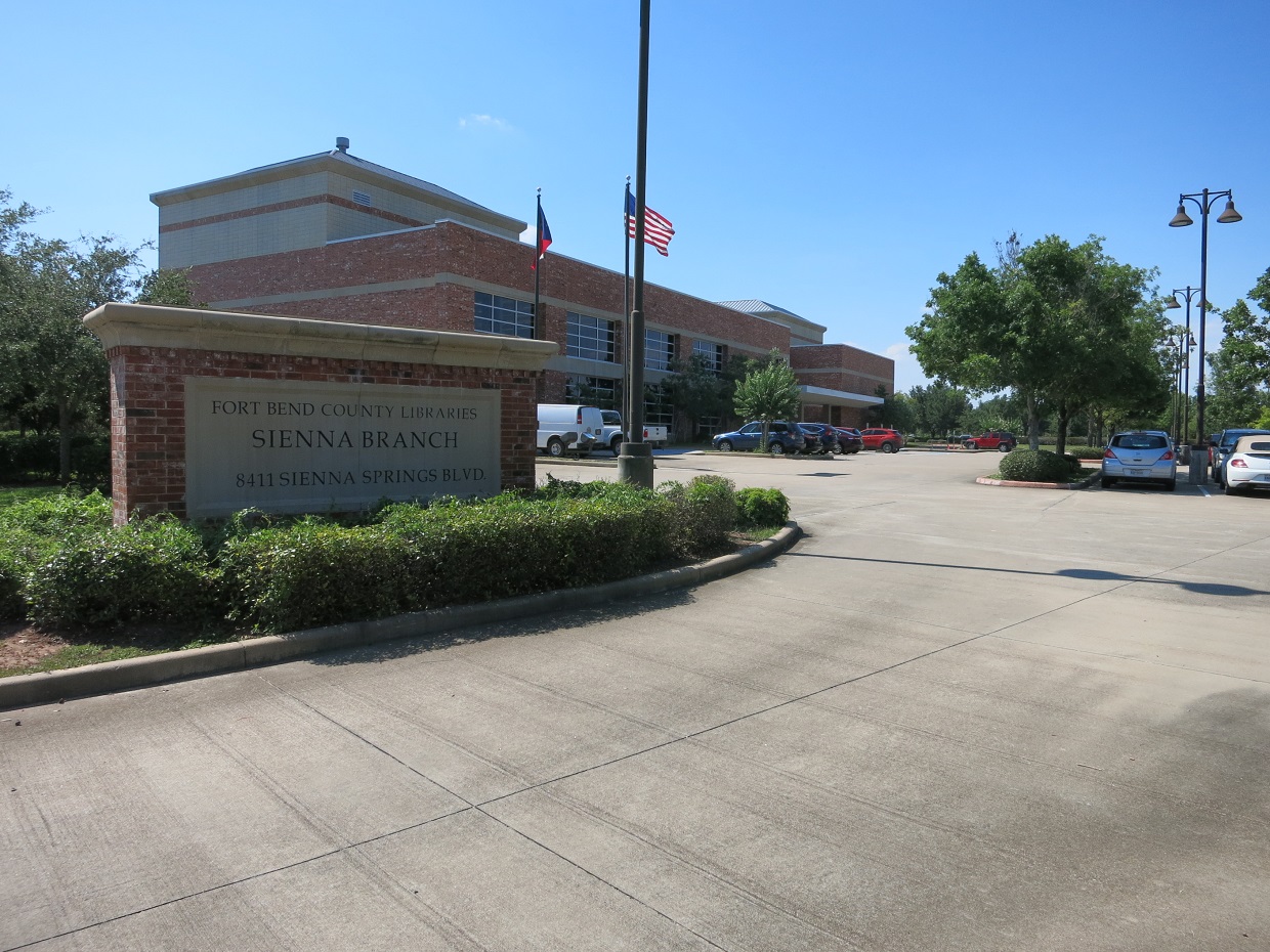 Two-story brick library building with flags and a monument sign in front.