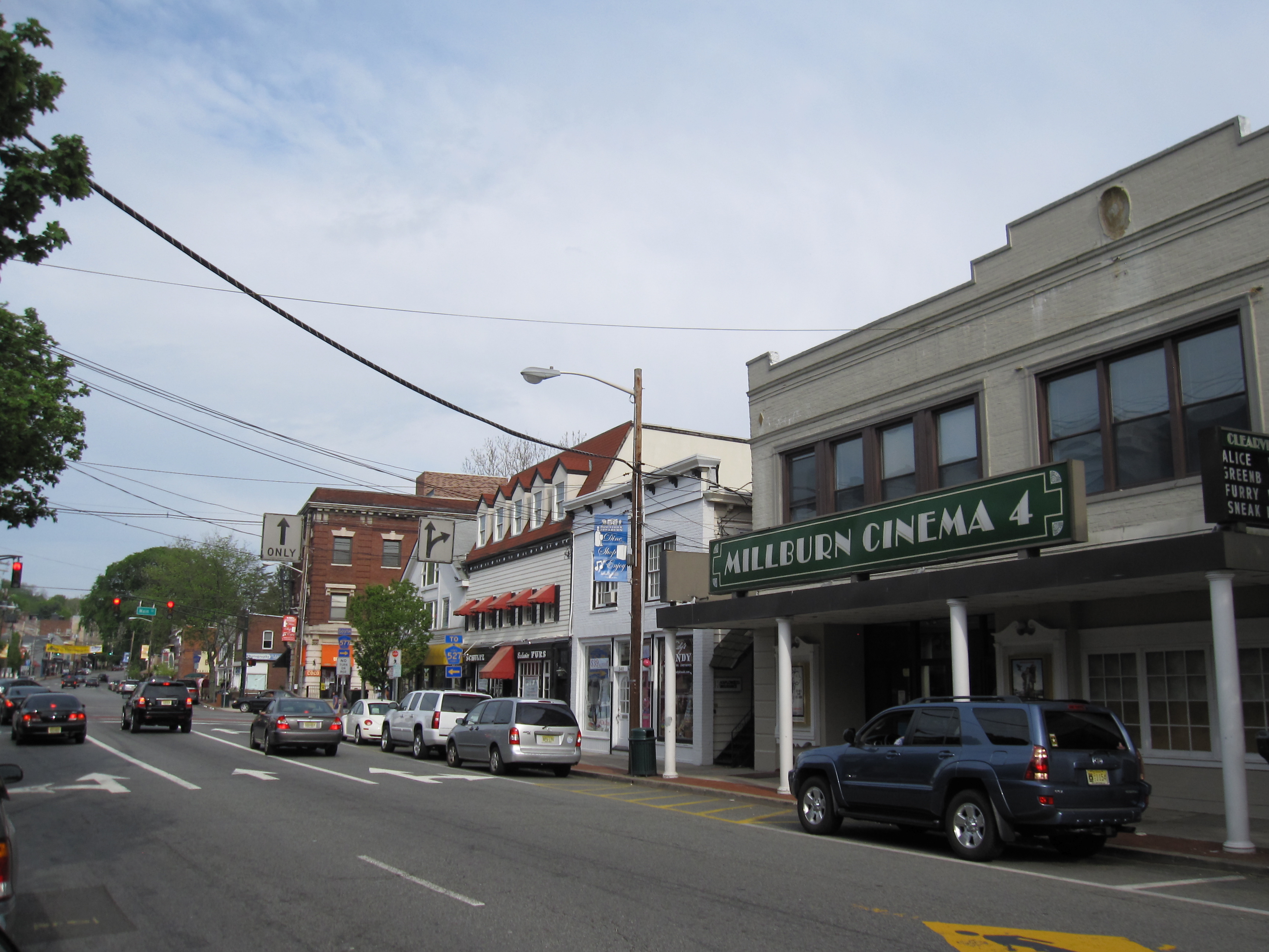 Downtown street lined with storefronts, parked cars, and a cinema marquee.