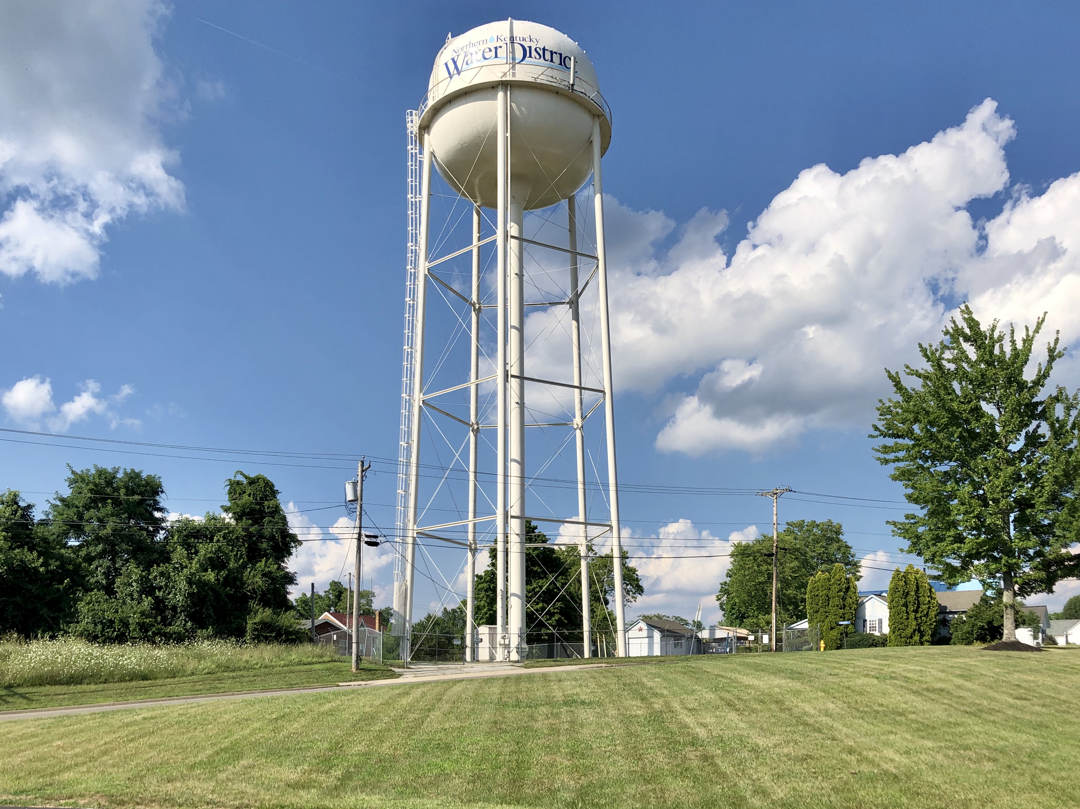 Tall white municipal water tower on a sunny day surrounded by grass and trees.