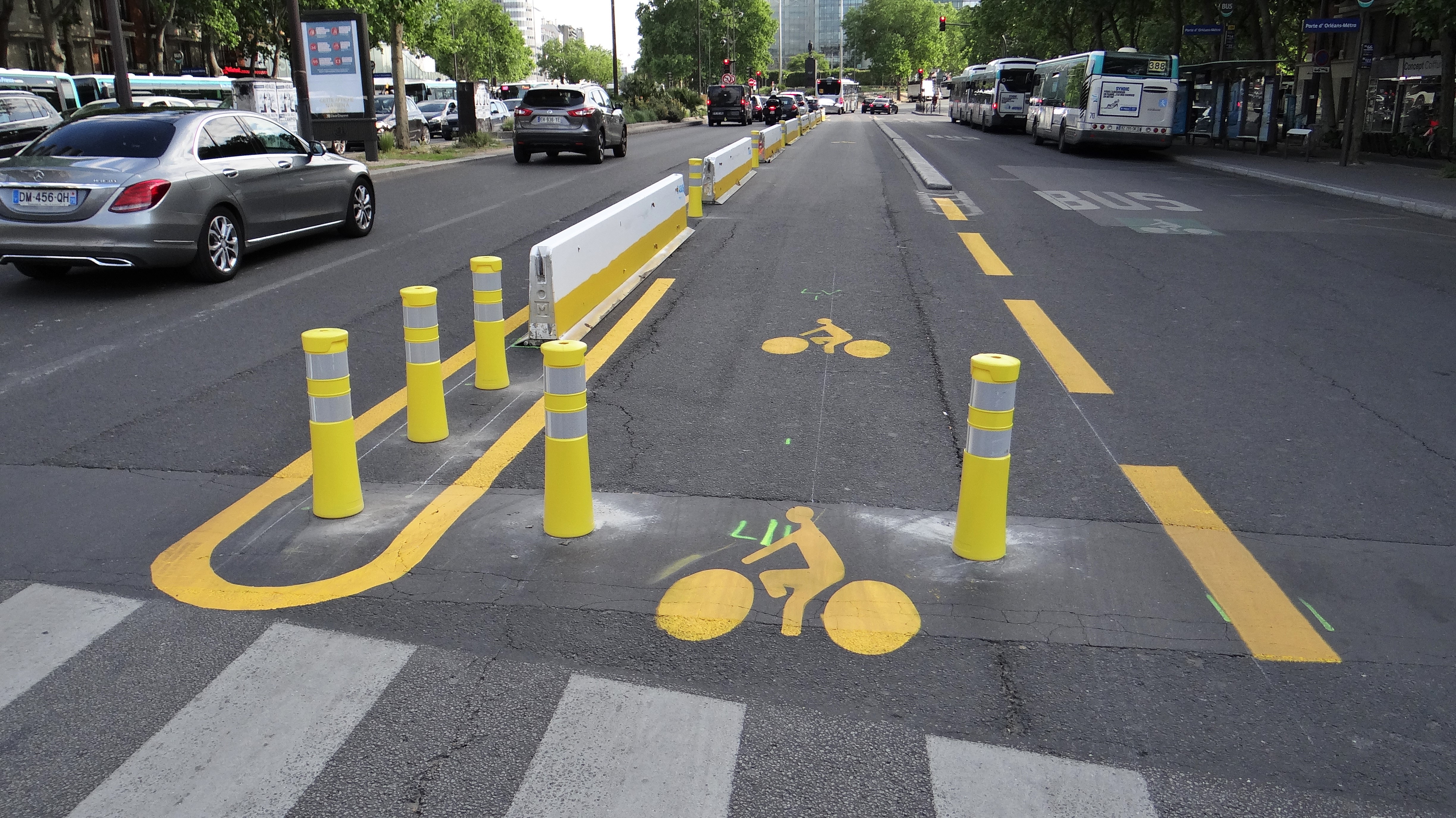 Yellow bollards and painted bicycle symbols mark a separated bike lane on a city street.