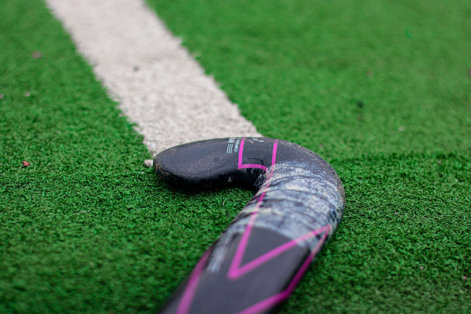 Detailed view of a field hockey stick on green artificial turf with white line.