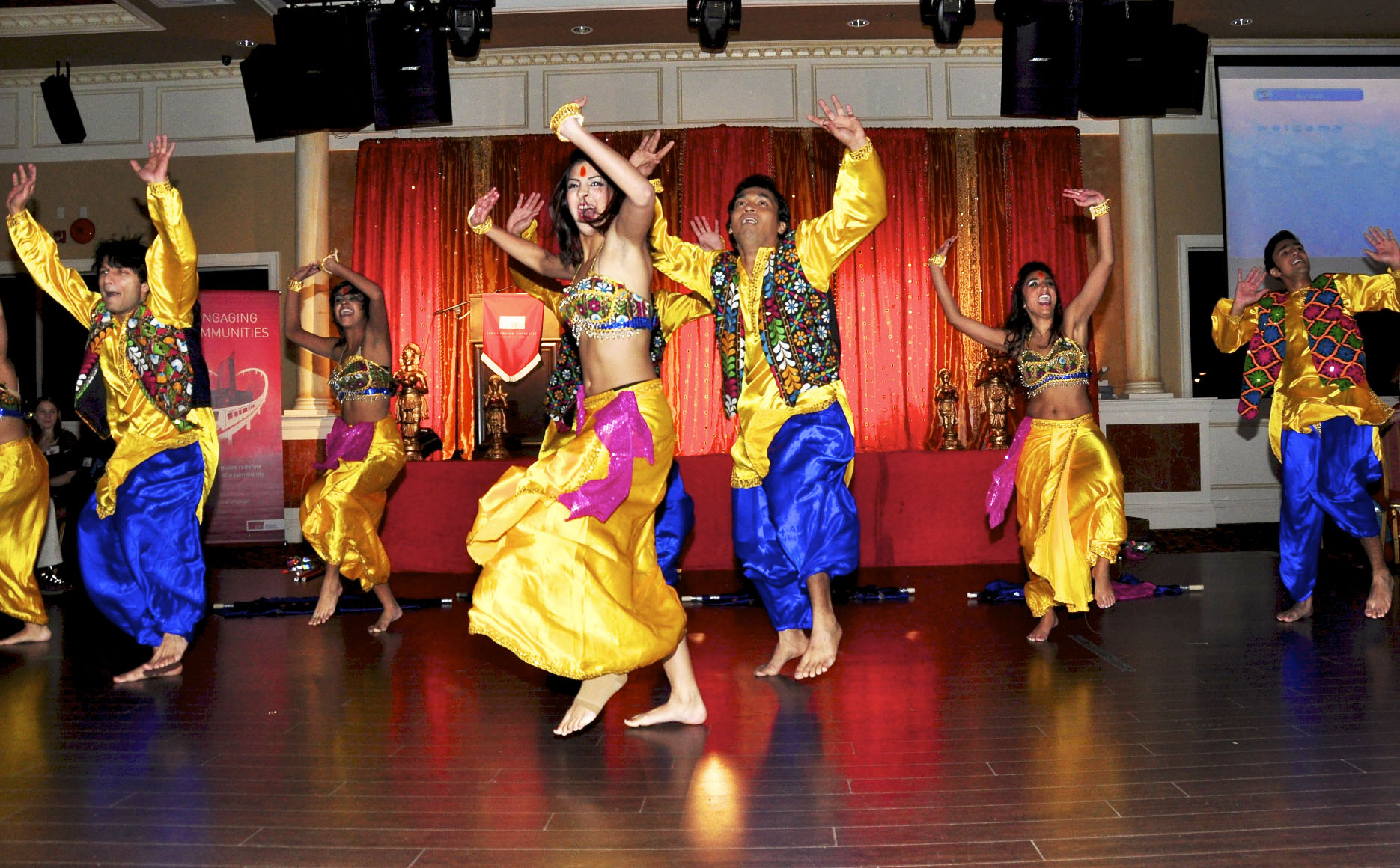 Dancers in colorful yellow and blue Indian costumes performing on a stage.