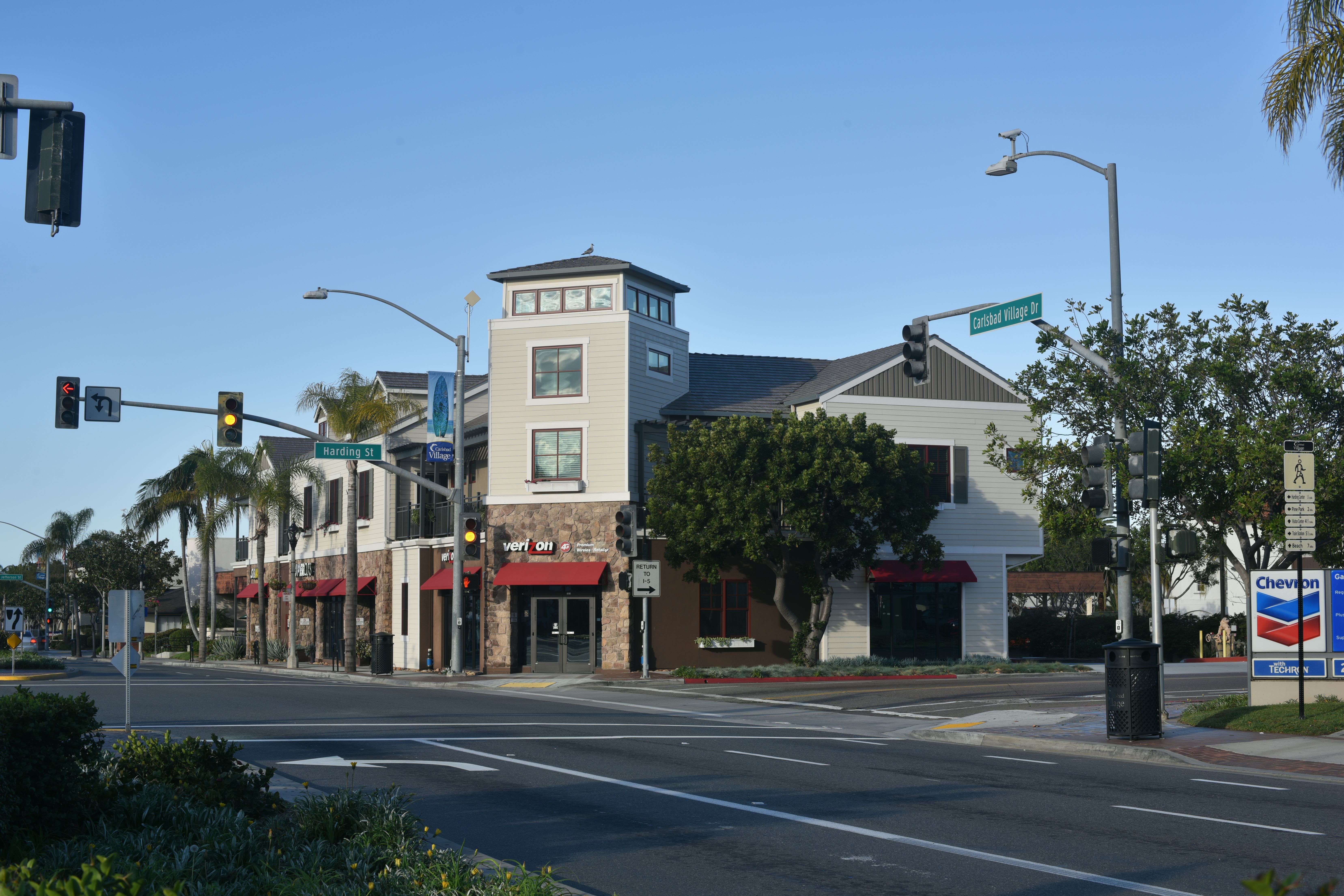 Street corner with retail stores, palm trees, and traffic signals on a sunny day.