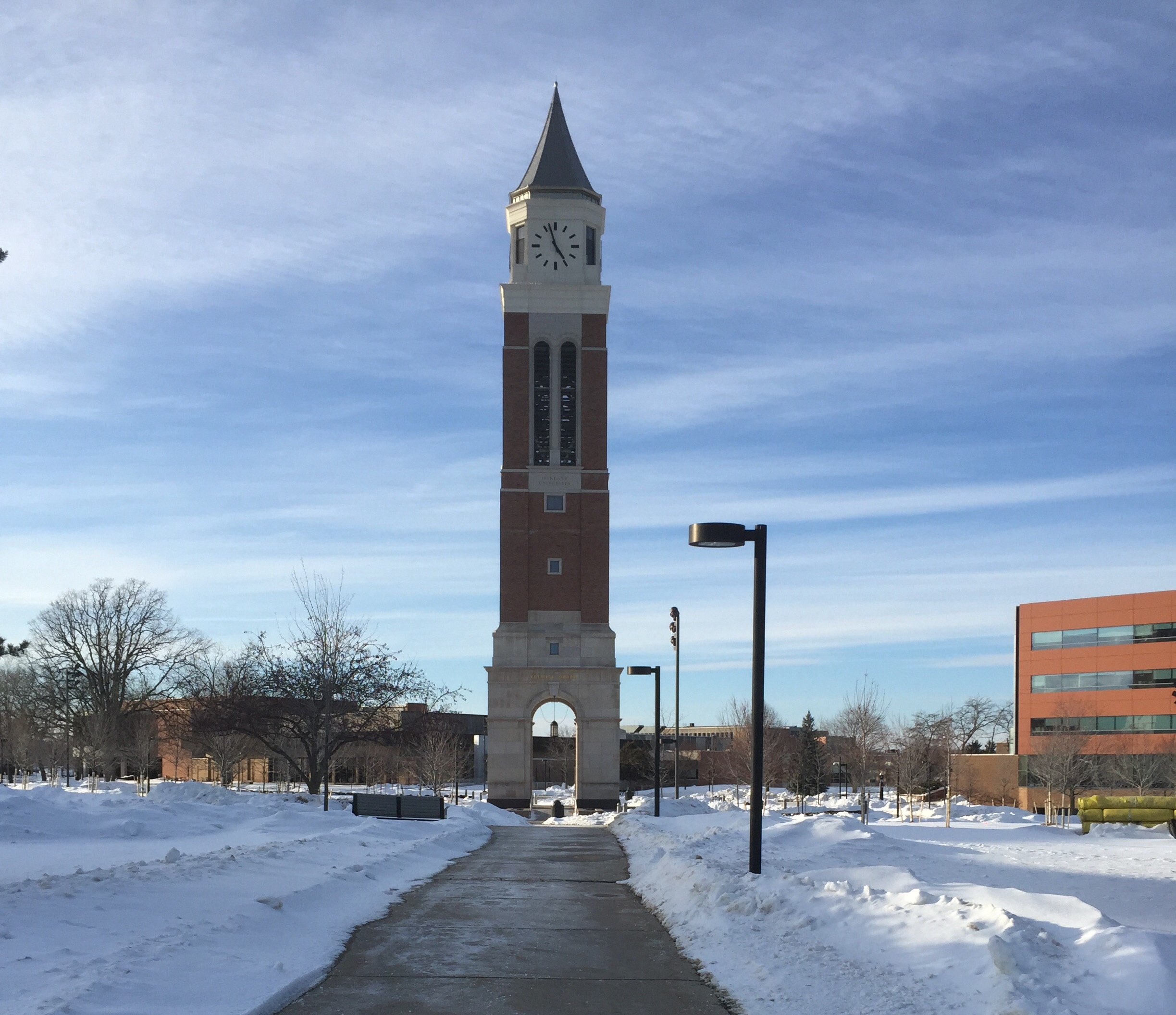 Tall brick carillon tower on a snow-covered university campus with a cleared walkway.