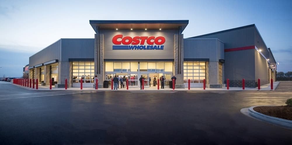 Costco Wholesale store exterior at dusk with red bollards and shoppers near the entrance.