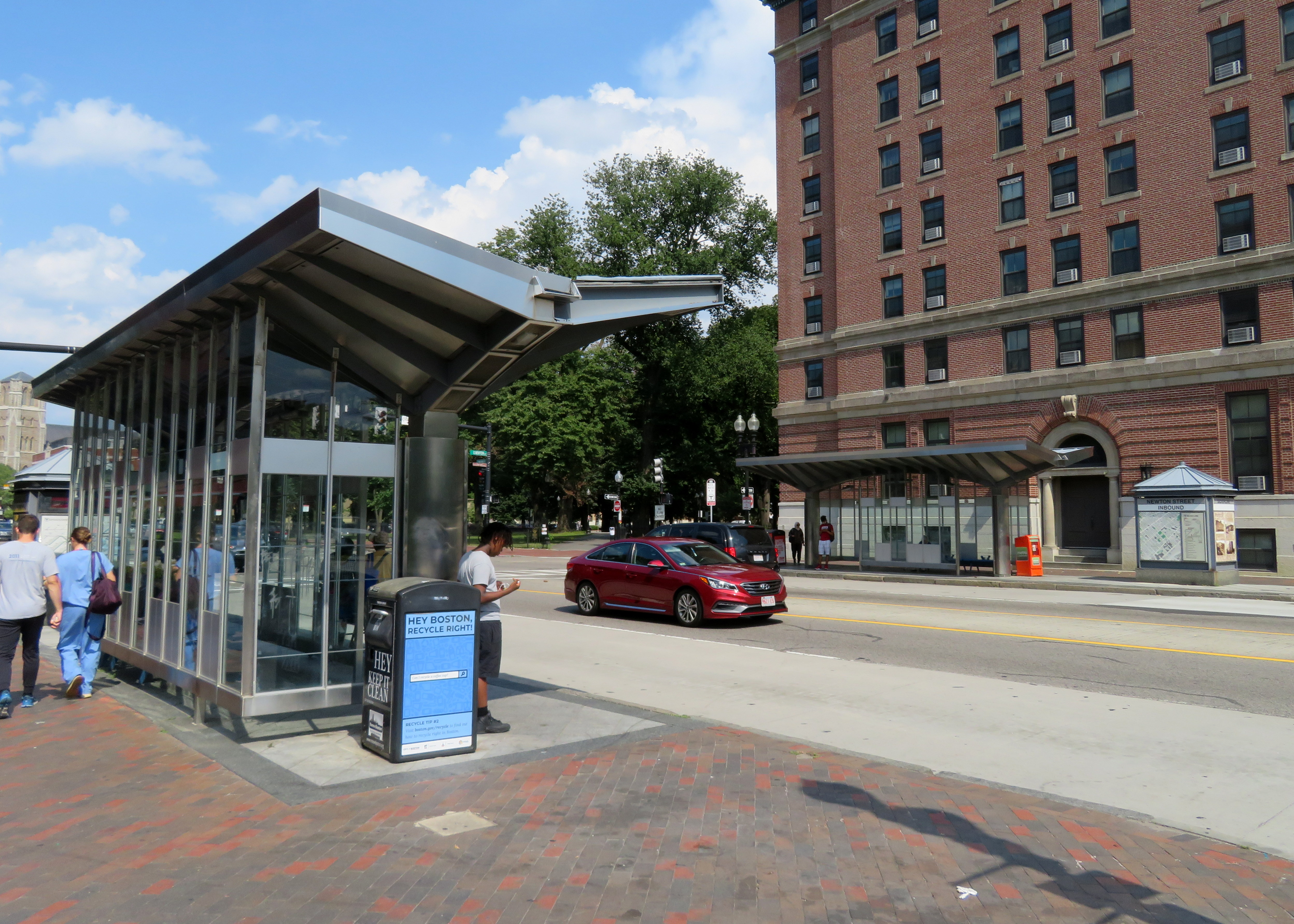 Two glass-and-steel bus shelters on a brick sidewalk along a city street.
