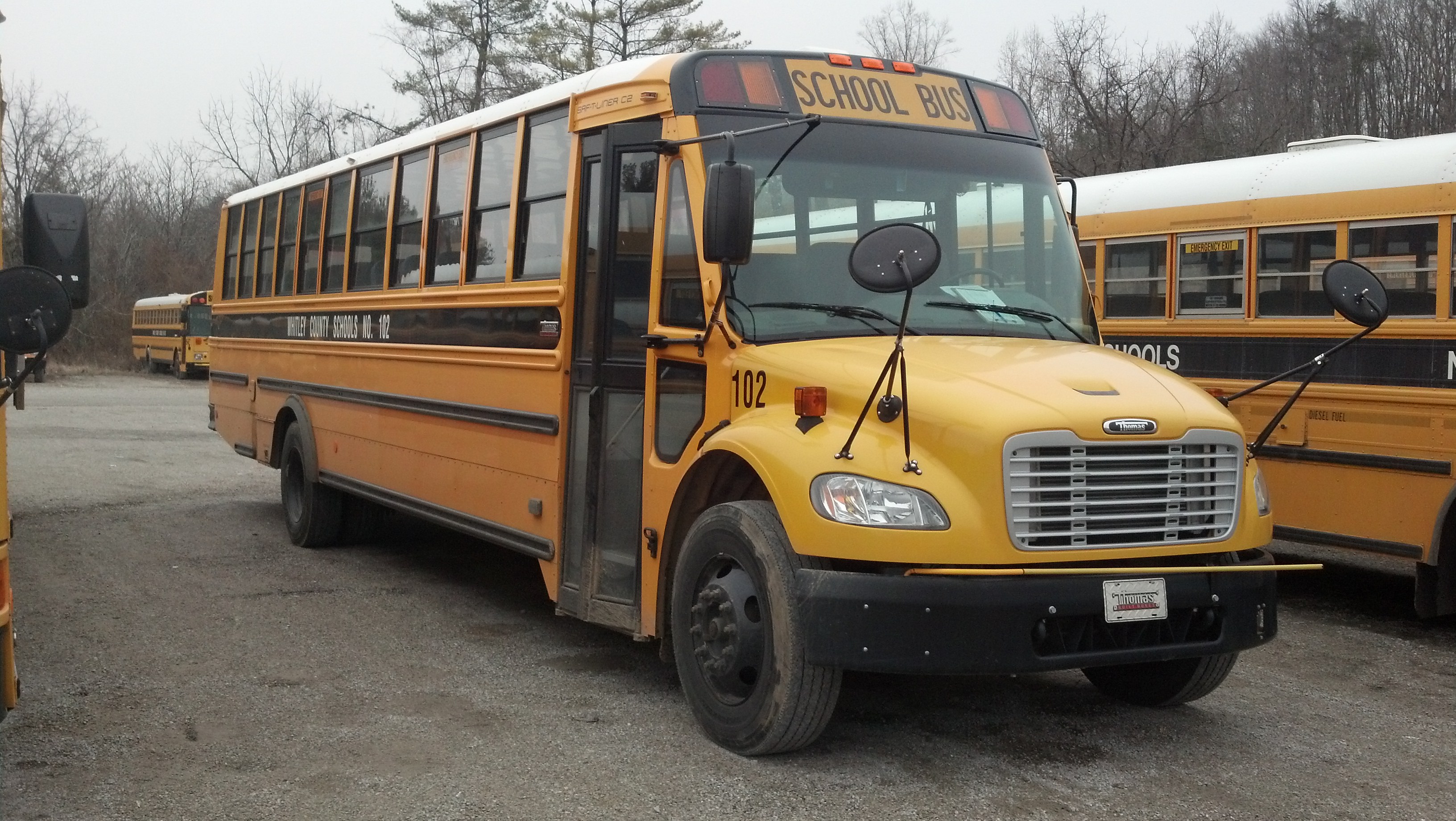 A yellow school bus parked in a depot lot with other buses behind it.