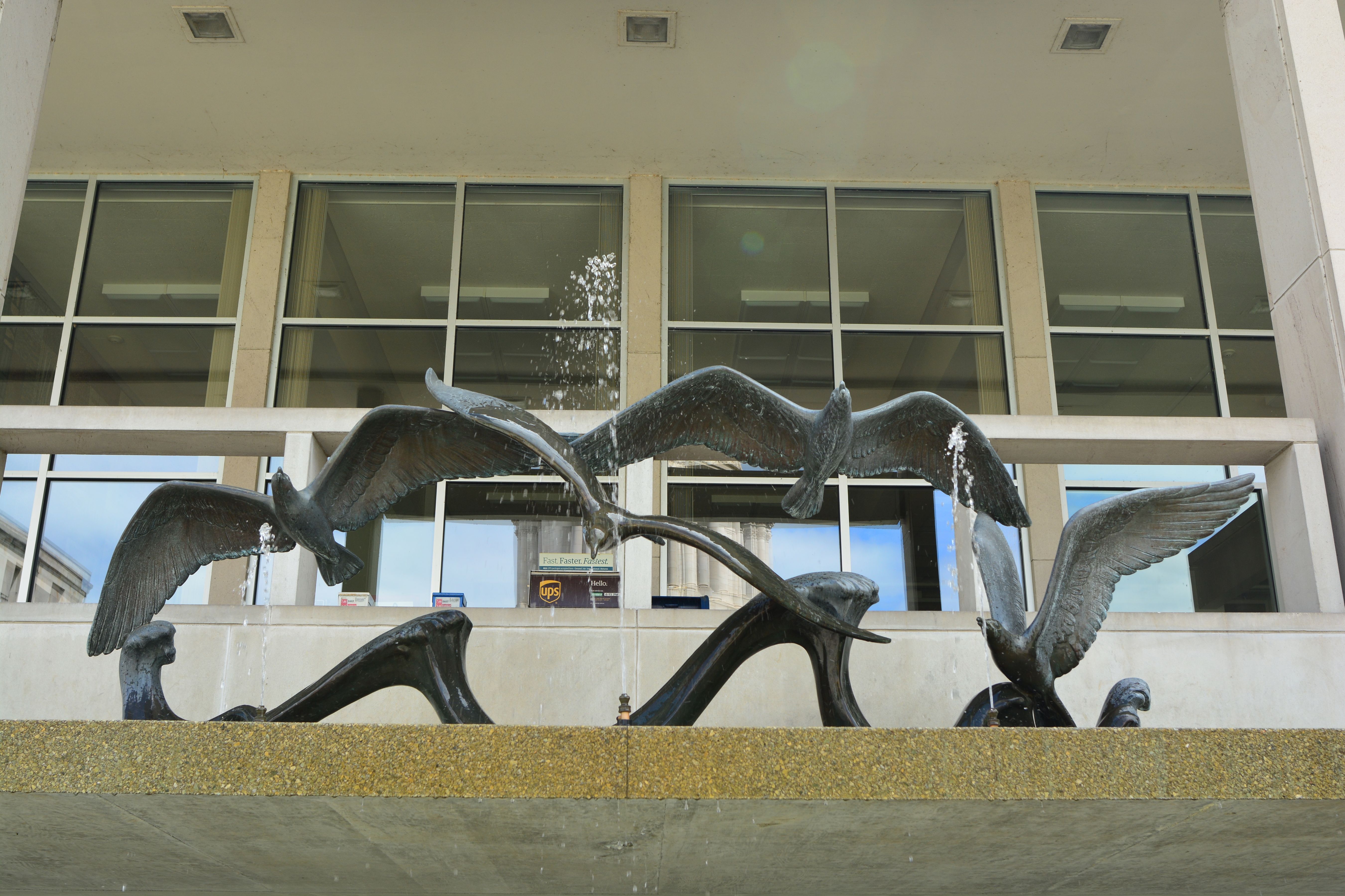 Bronze bird sculptures of the Du Pen Fountain in front of a modernist glass government building.
