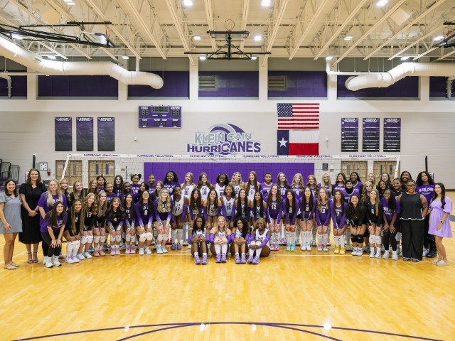 Large group of volleyball players in purple uniforms posed in a gymnasium.