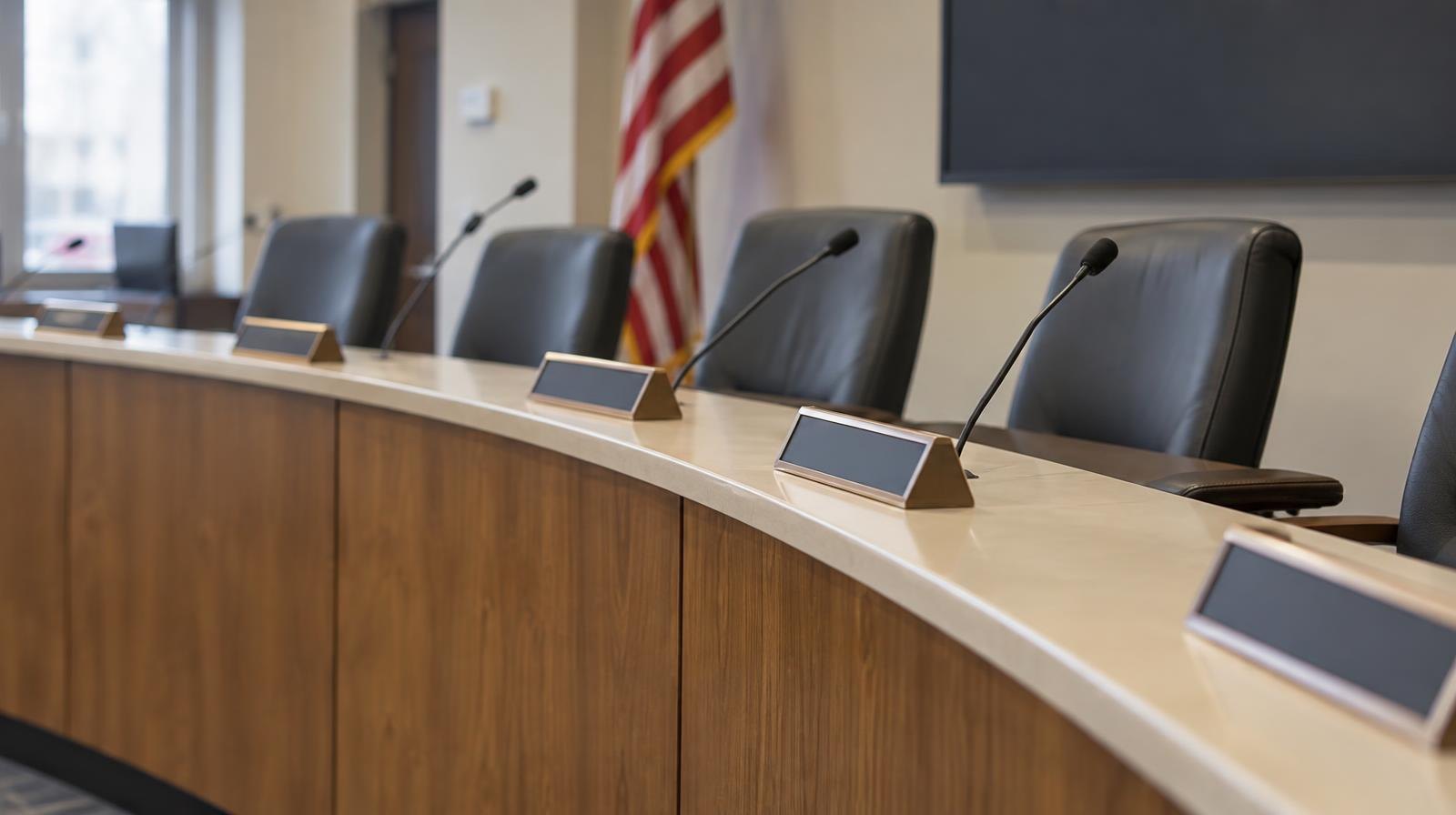 Empty school board meeting room with a curved dais, name placards, and microphones.