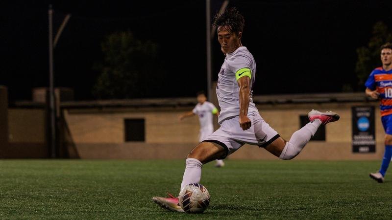 A soccer player in a white uniform prepares to kick a ball on a lit turf field at night.