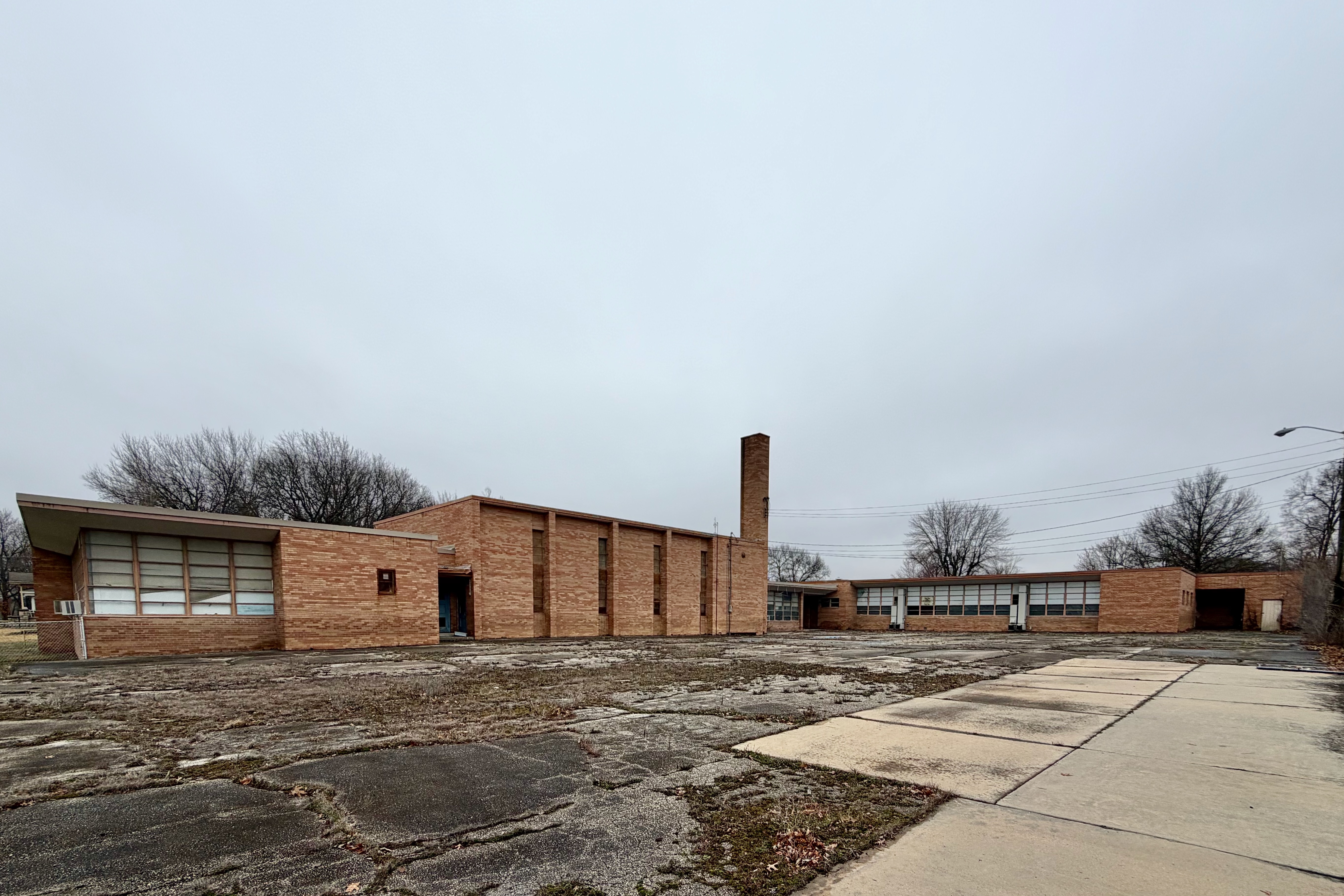 Exterior of a low-rise brick elementary school building with a tall chimney.
